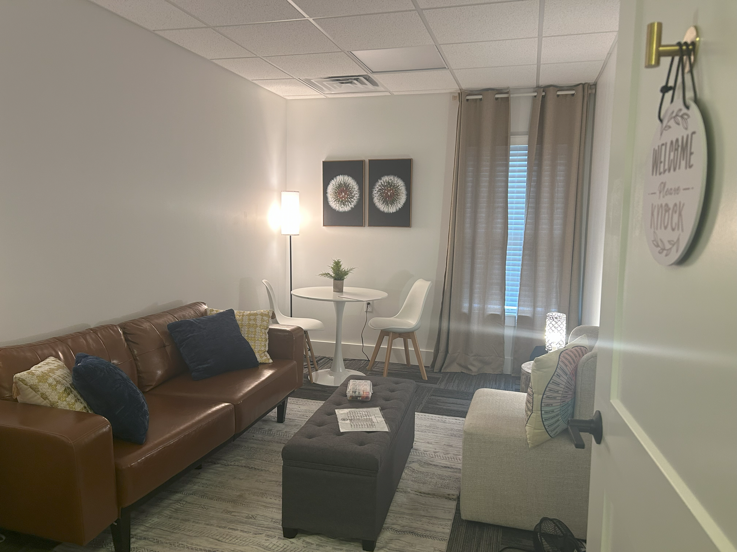 cozy office with a couch, chair, ottoman, floor lamp, bistro table, and paintings