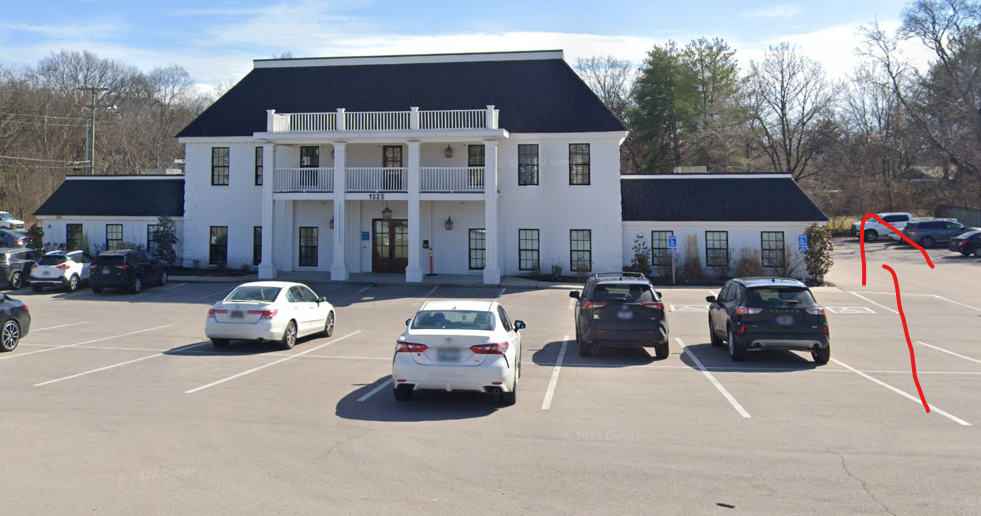large white building with cars parked out front in a big parking lot