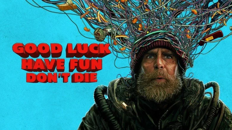 A man wearing a red beanie and a futuristic costume is engulfed by a whirlwind of cables and cheetos. In red text the title says "good luck have fun don't die"