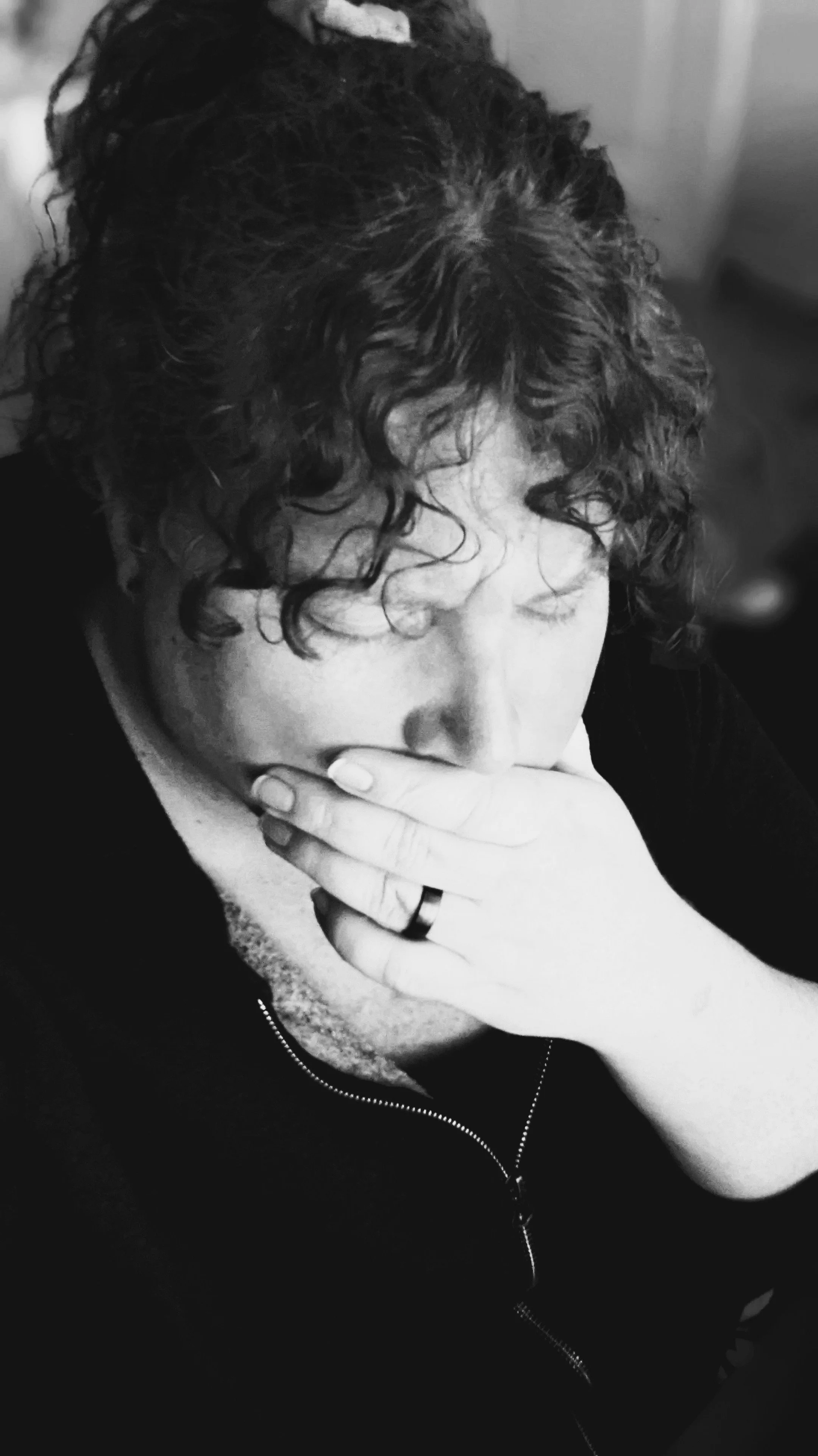 A high contrast black and white image of a woman holding her hand over her mouth with her eyes closed, showing anguish