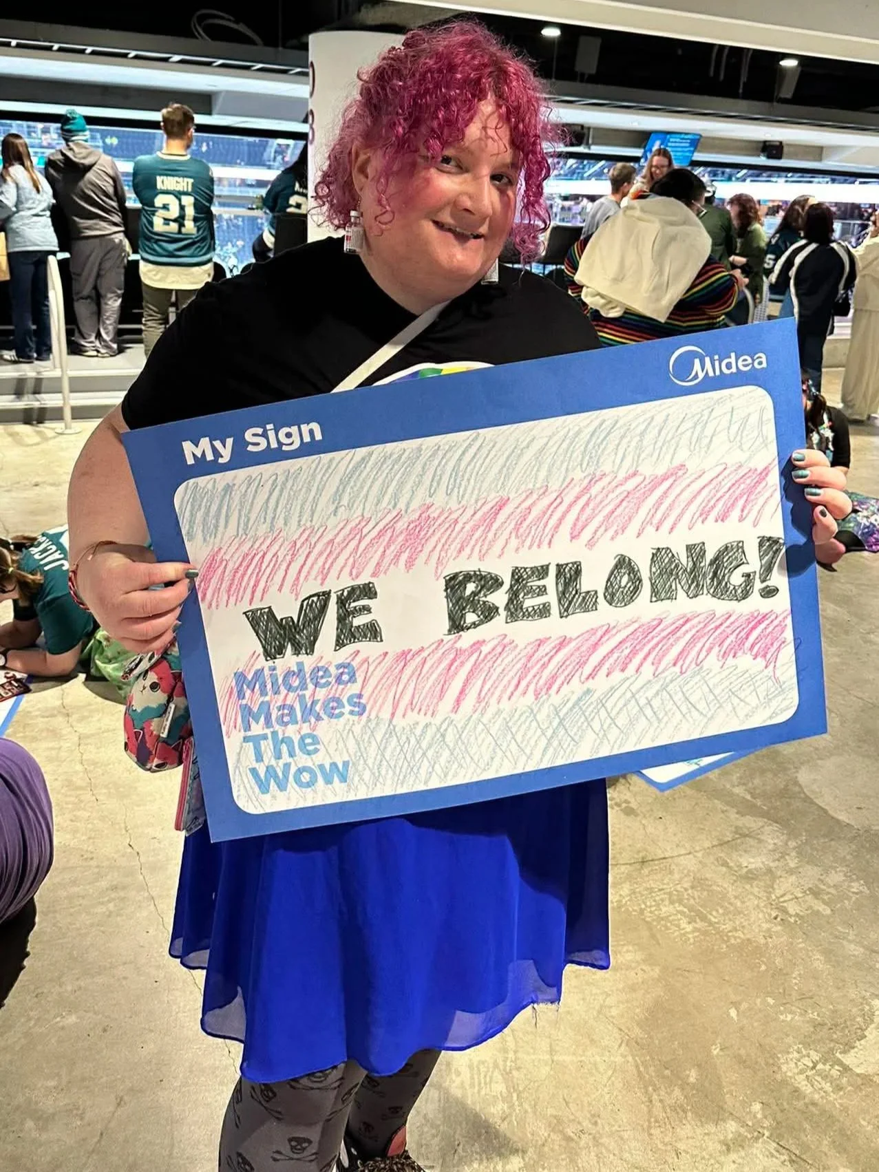 Transgender life coach Hazel Bloom holding a trans pride sign that says "we belong!" While wearing a really cute outfit