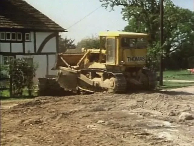a yellow bulldozer knocking down a brick gate in front of an old english house
