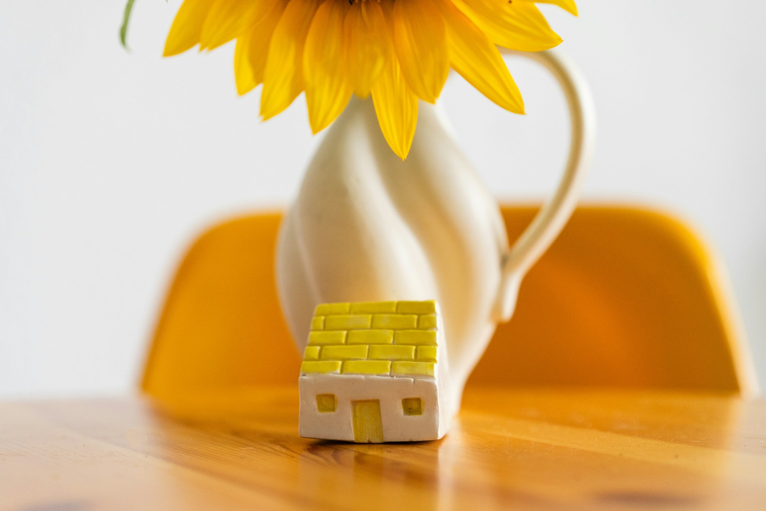 Close-up of a small, yellow and white toy figure with yellow stairs in the foreground, a white figure with drooping ears, and a yellow flower petal. The background is blurred with yellow and white tones.