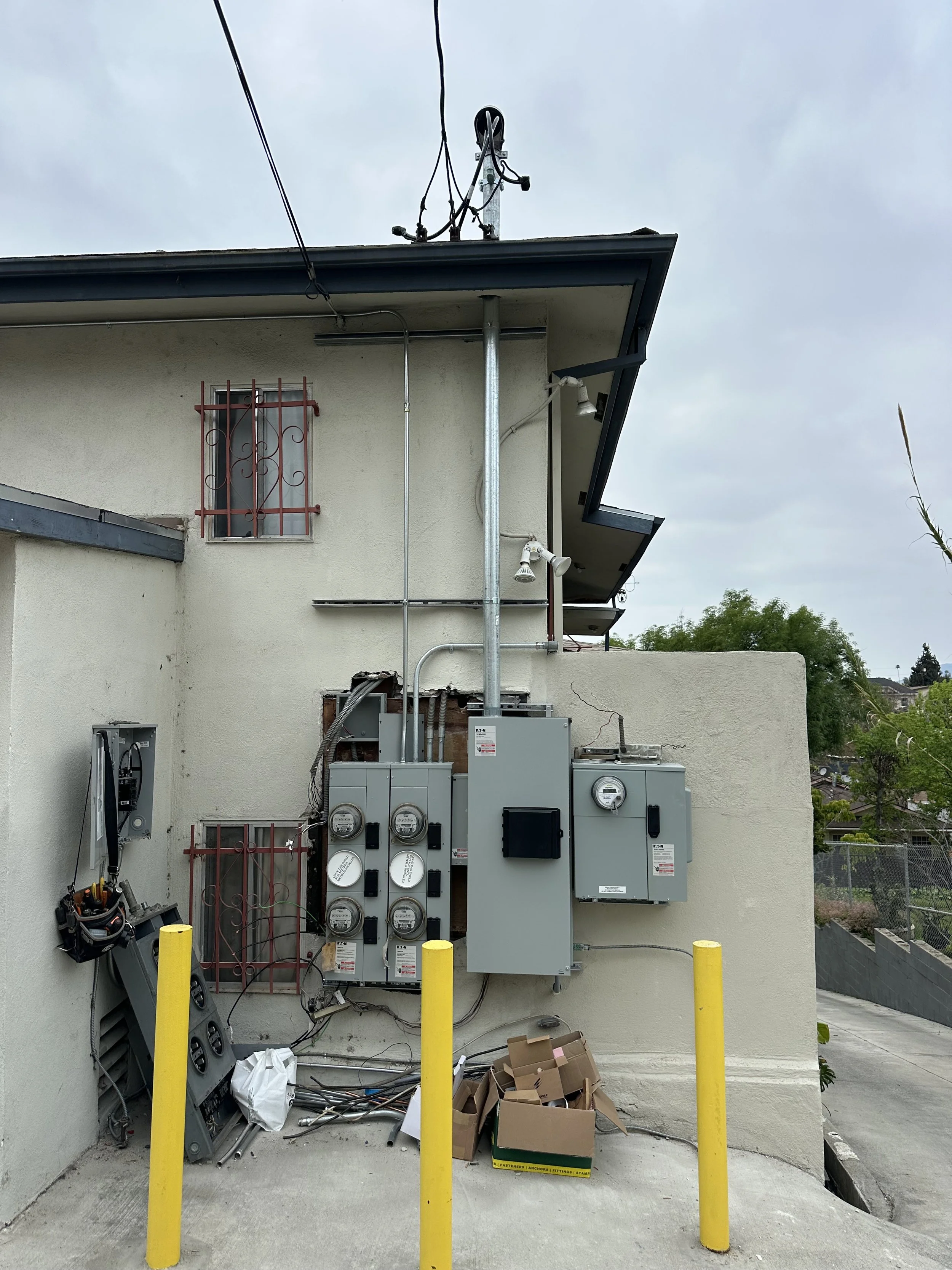 Electrical equipment and meters installed on the side of a building with yellow safety poles in front.