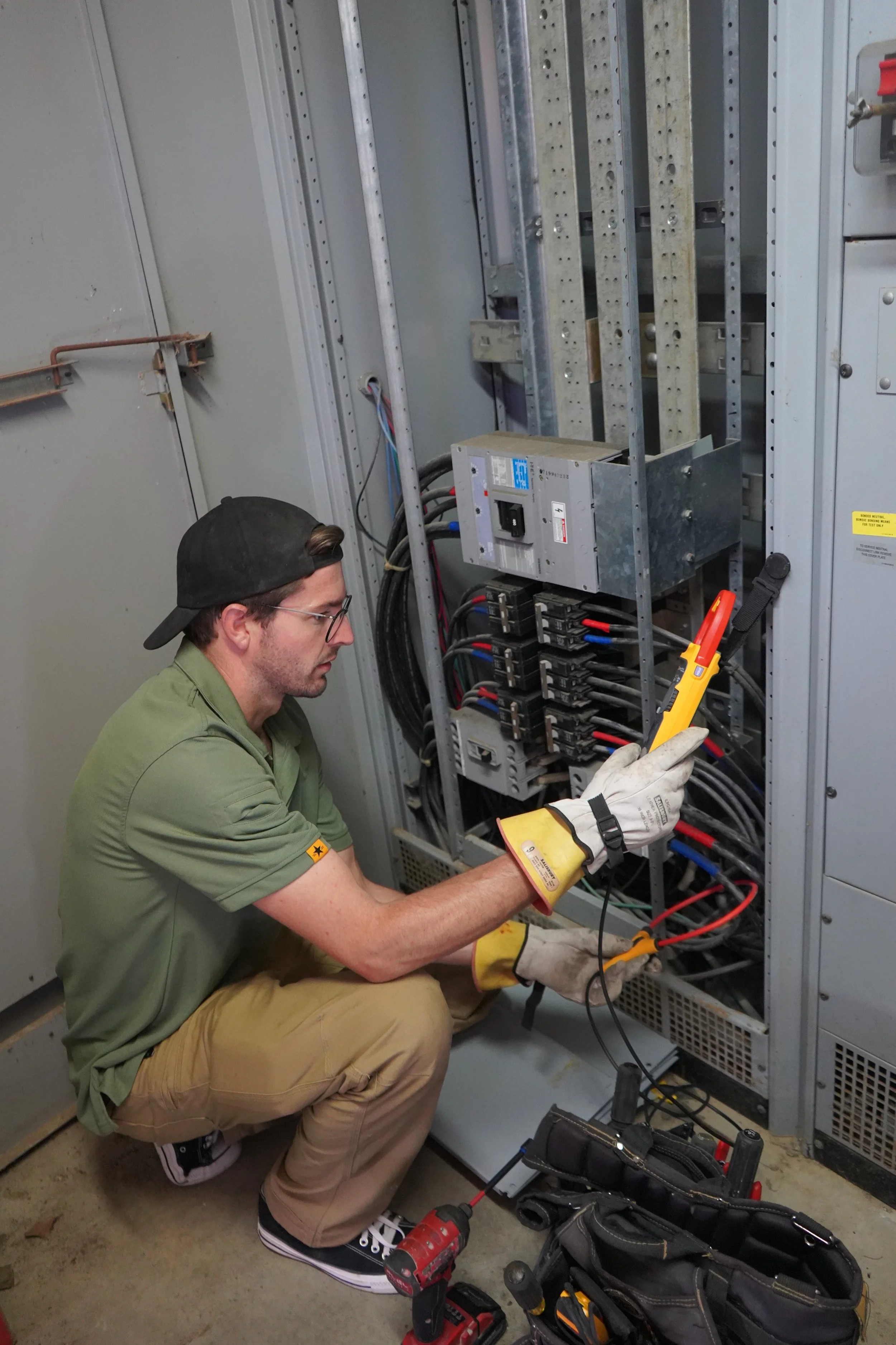 A technician inspecting electrical components inside an electrical panel, using a multimeter.