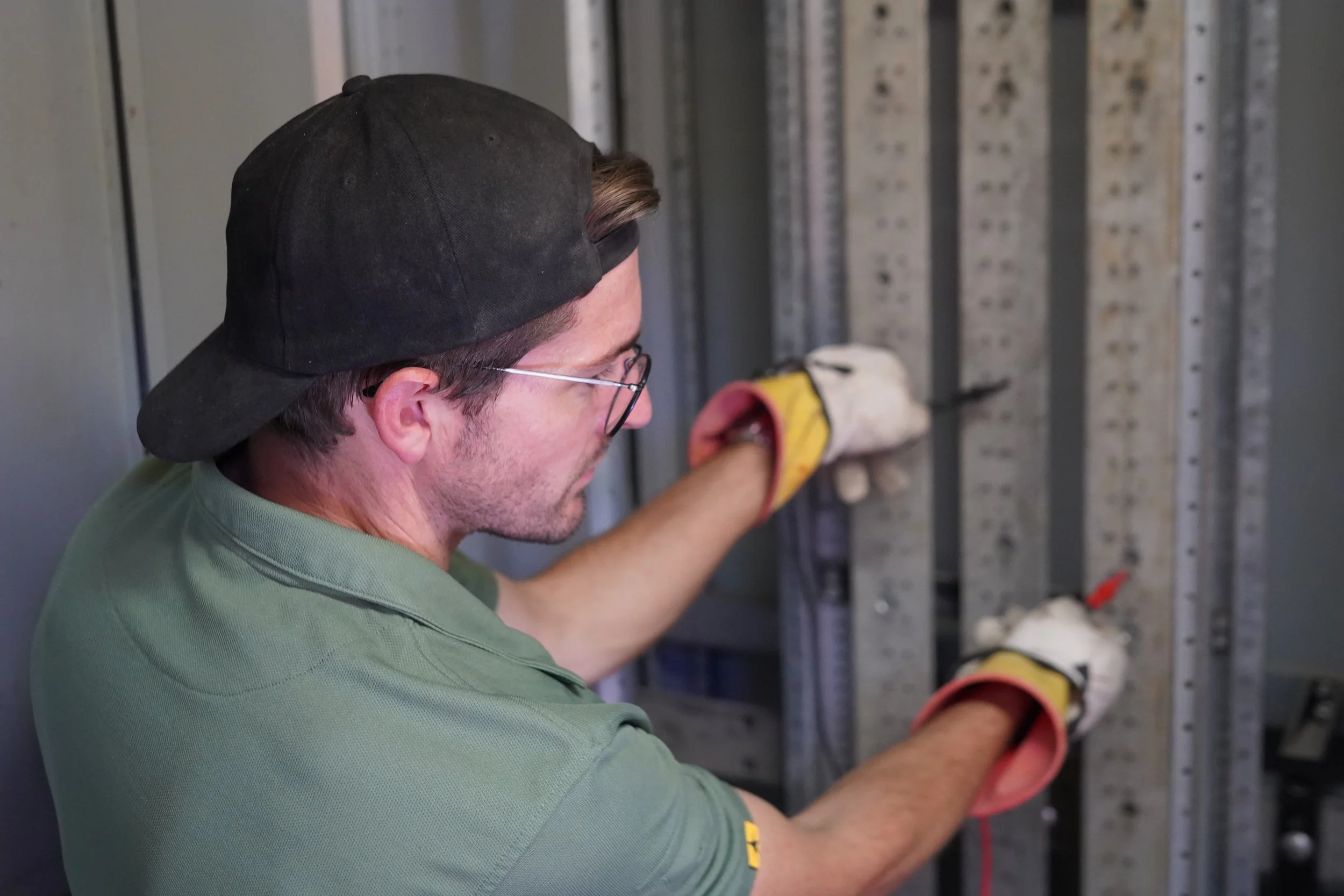 An electrician working on electrical wiring inside a panel, wearing safety gloves.