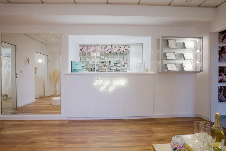 Ein weißer Empfangstresen mit einer hinter ihm angebrachten Dekoration aus lilafarbenen und rosa Blumen sowie einem Neon-Schriftzug "say yes".