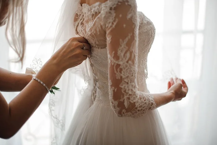 Eine Braut wird während der Vorbereitung an ihrem Brautkleid geholfen.