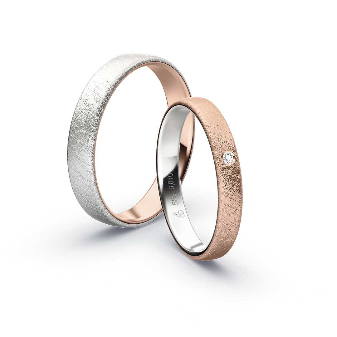 Zwei Eheringe, einer silberfarben mit einem Diamanten, der andere roségoldfarben, mit einem strukturierten Muster.