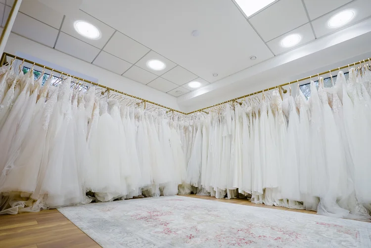 Ein Raum voller weißer Brautkleider, die an goldfarbenen Kleiderstangen hängen, wahrscheinlich in einem Brautmodengeschäft.