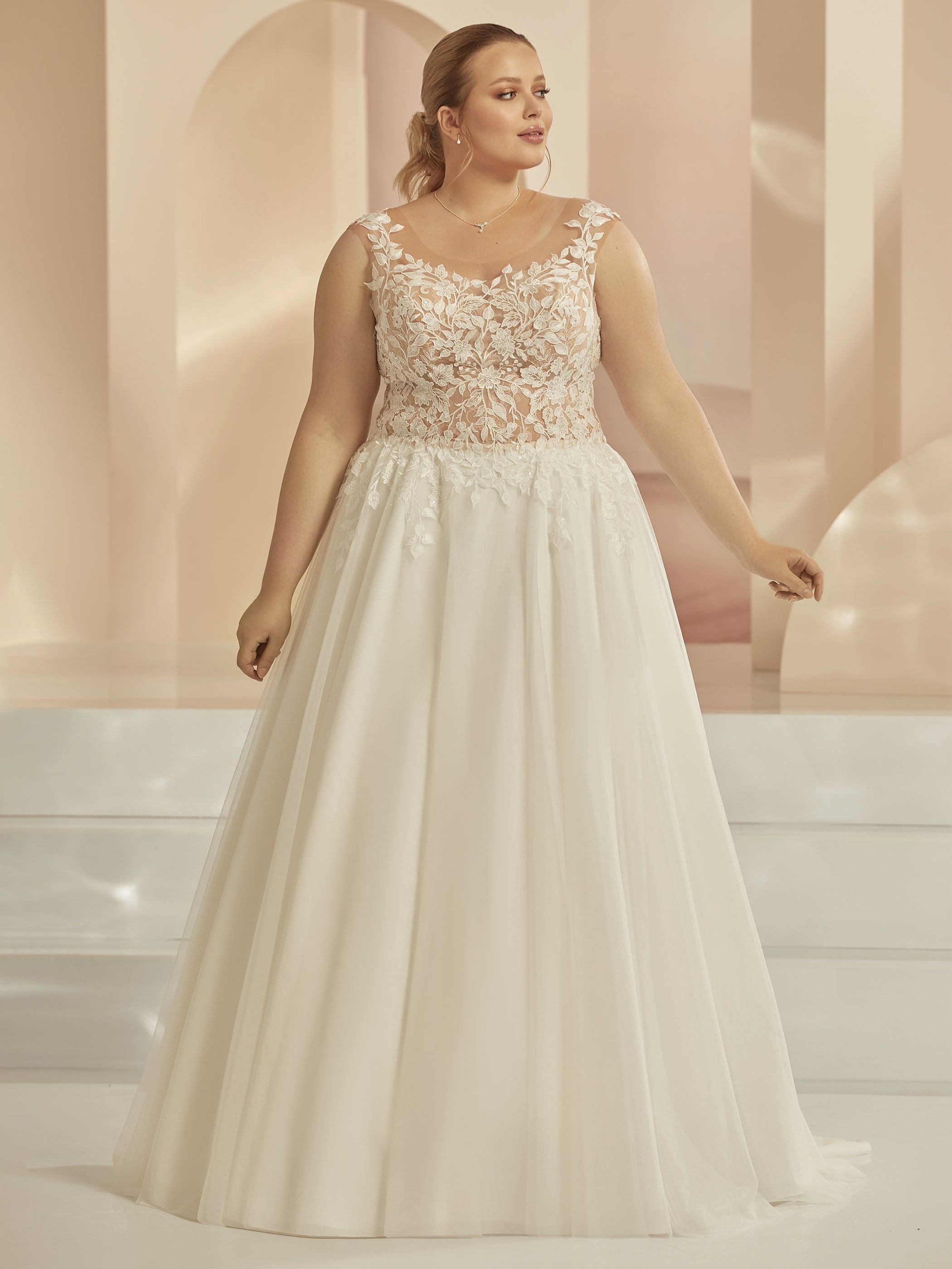 Frau im eleganten Brautkleid mit Spitze im Oberteil, Hintergrund in Pastelltönen.