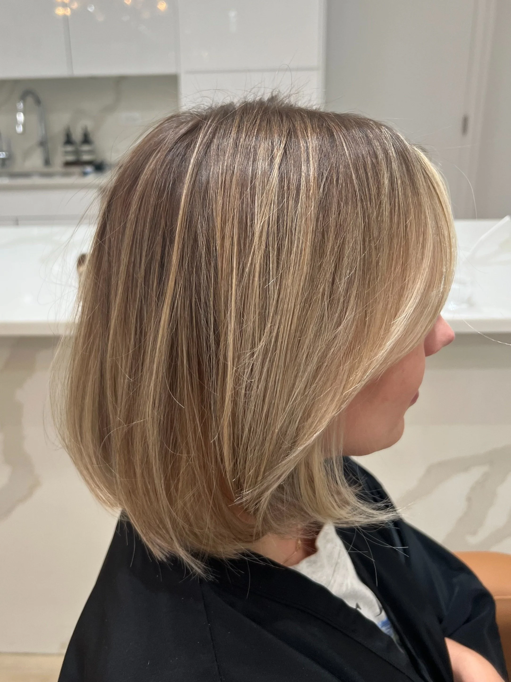 Woman with blonde shoulder-length hair sitting in a salon, side profile view.