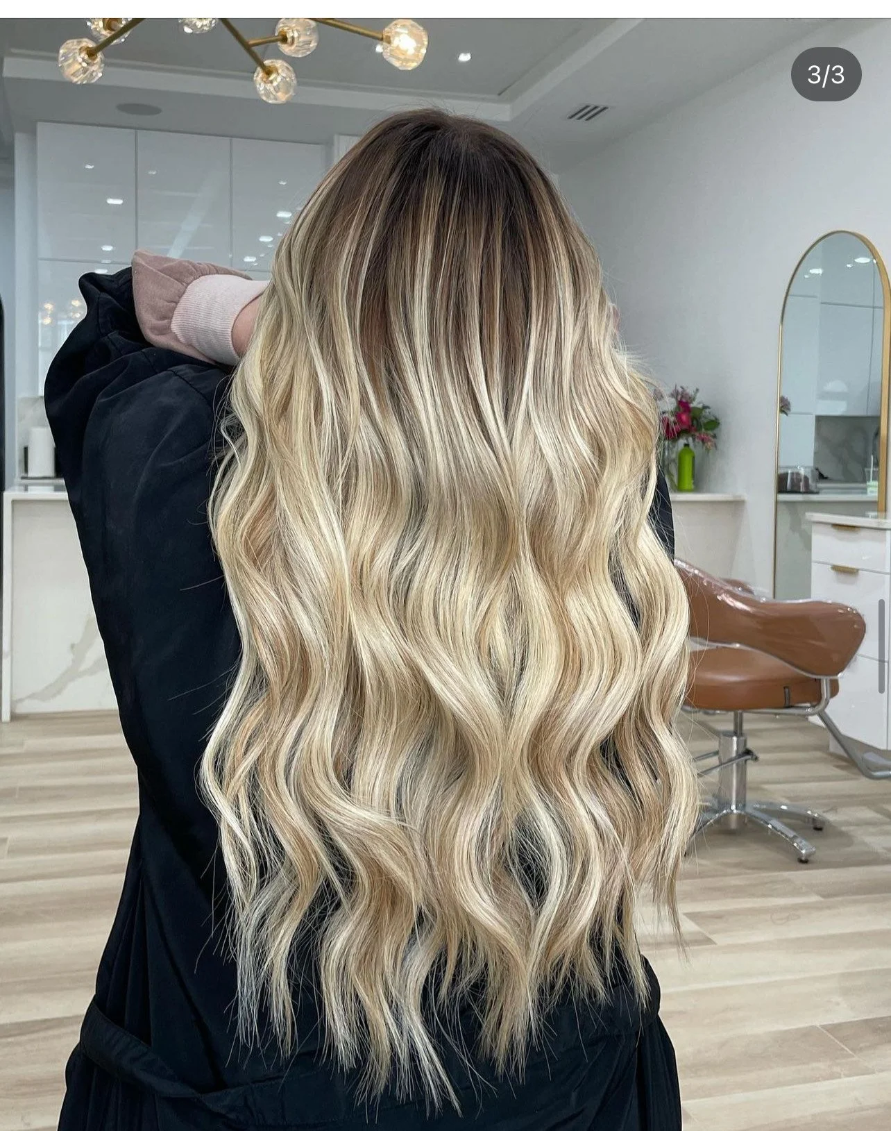 Person with long, wavy blonde hair facing away in a salon setting.