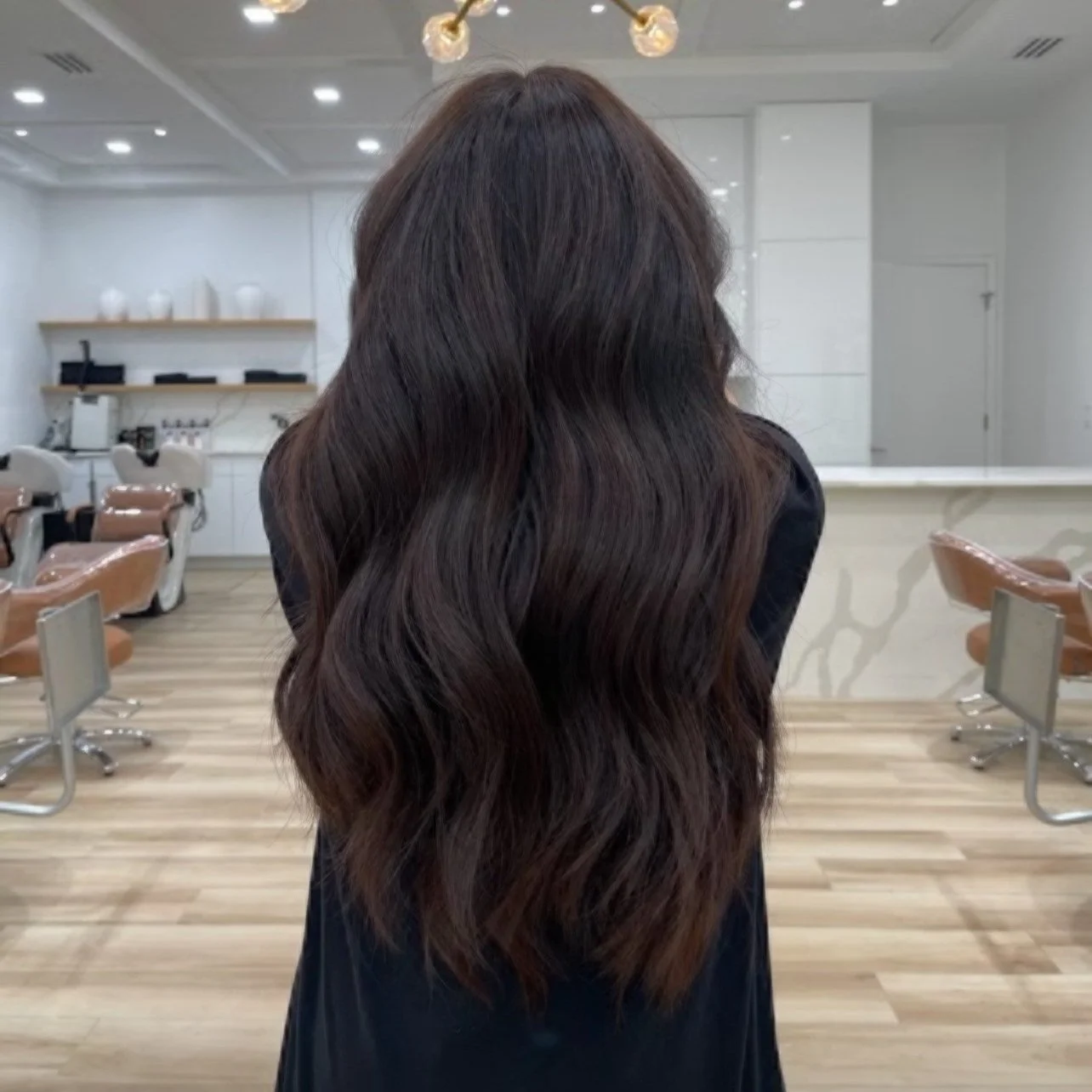 Person with long, wavy black hair in a salon setting
