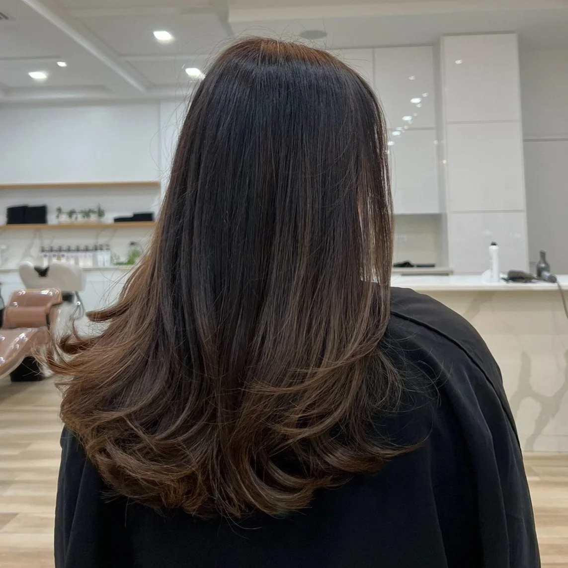 Person with long brown hair inside a modern hair salon