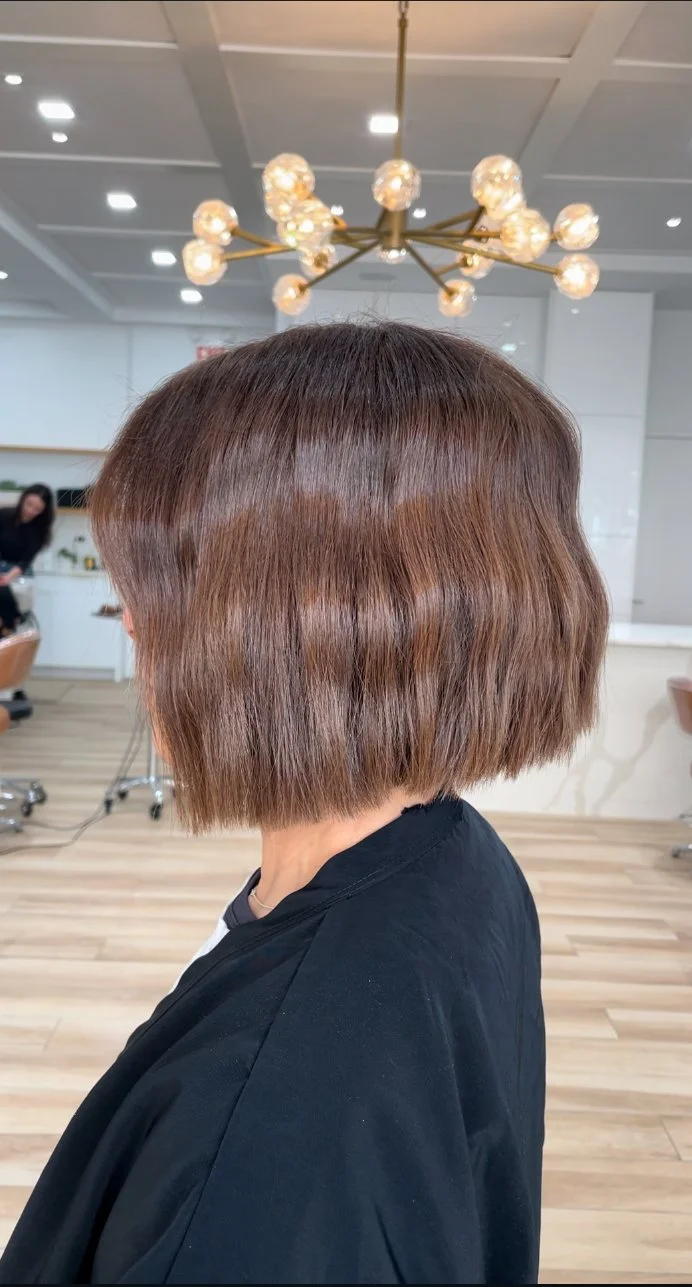 Woman with a straight, chin-length, layered bob hairstyle with a subtle reddish-brown color, seated in a salon.