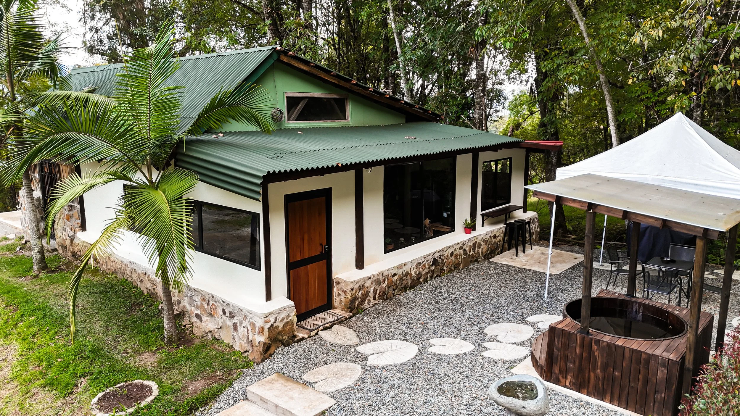 Rustic cabin exterior green roof white walls palm trees courtyard Equilibrium Jericó Colombia