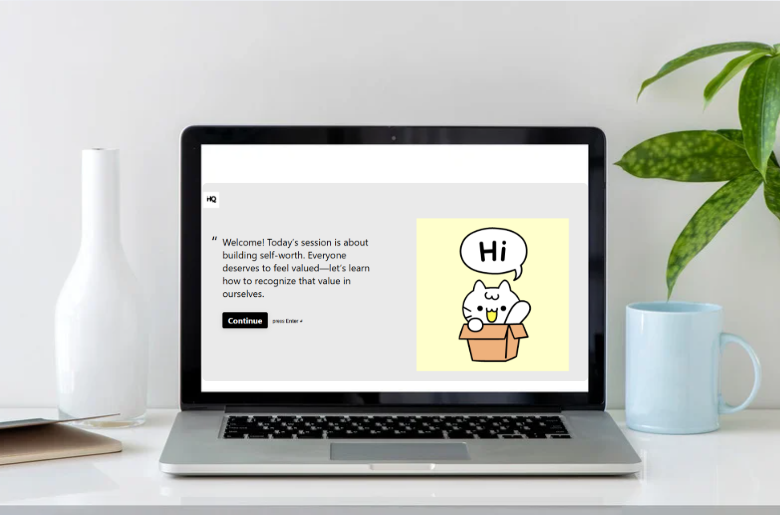 Laptop on a white desk displaying a welcome message and a cartoon cat with a speech bubble saying 'Hi.'