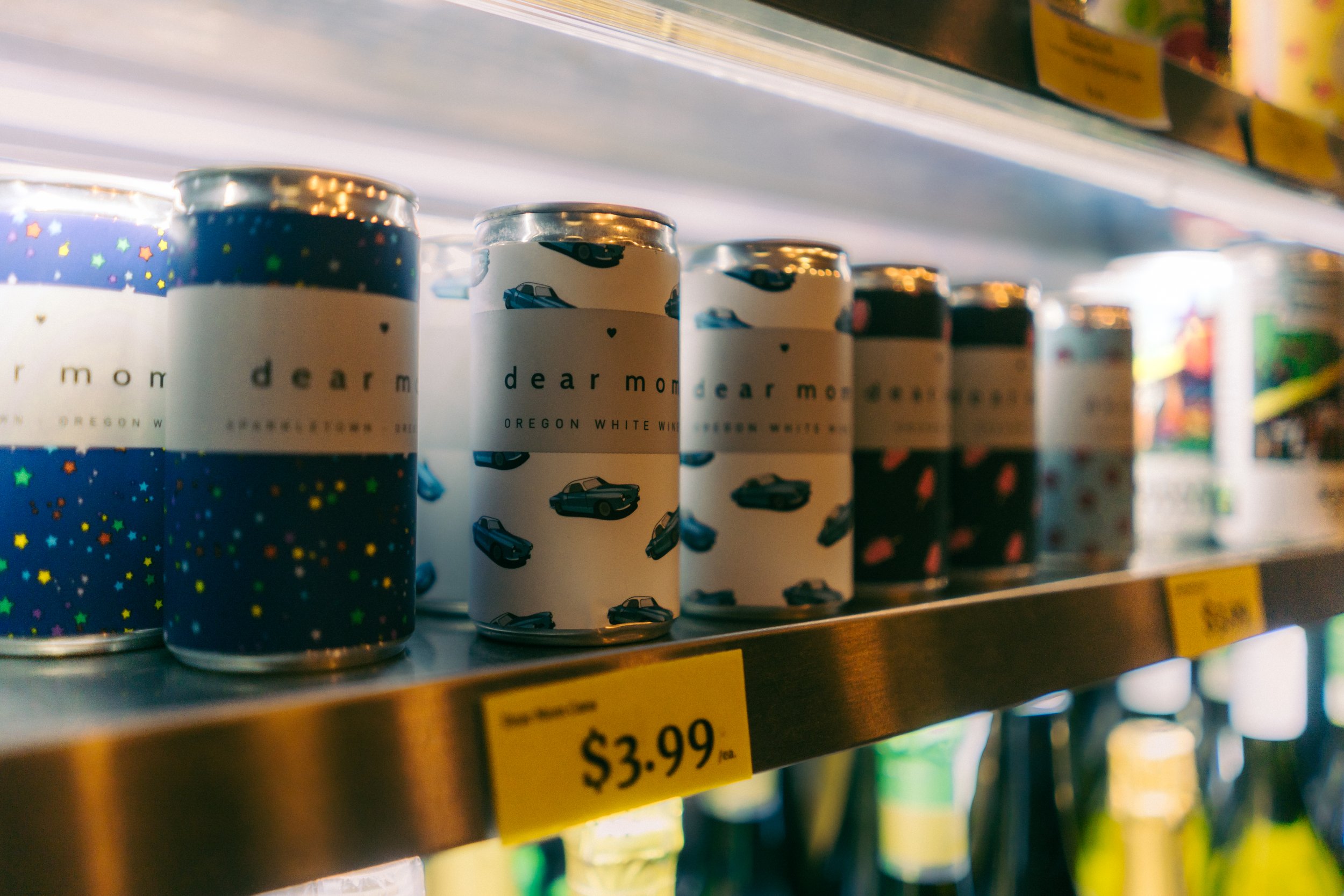 Cans of Dear Mom Oregon White Wine on store shelf, priced at $3.99 each.