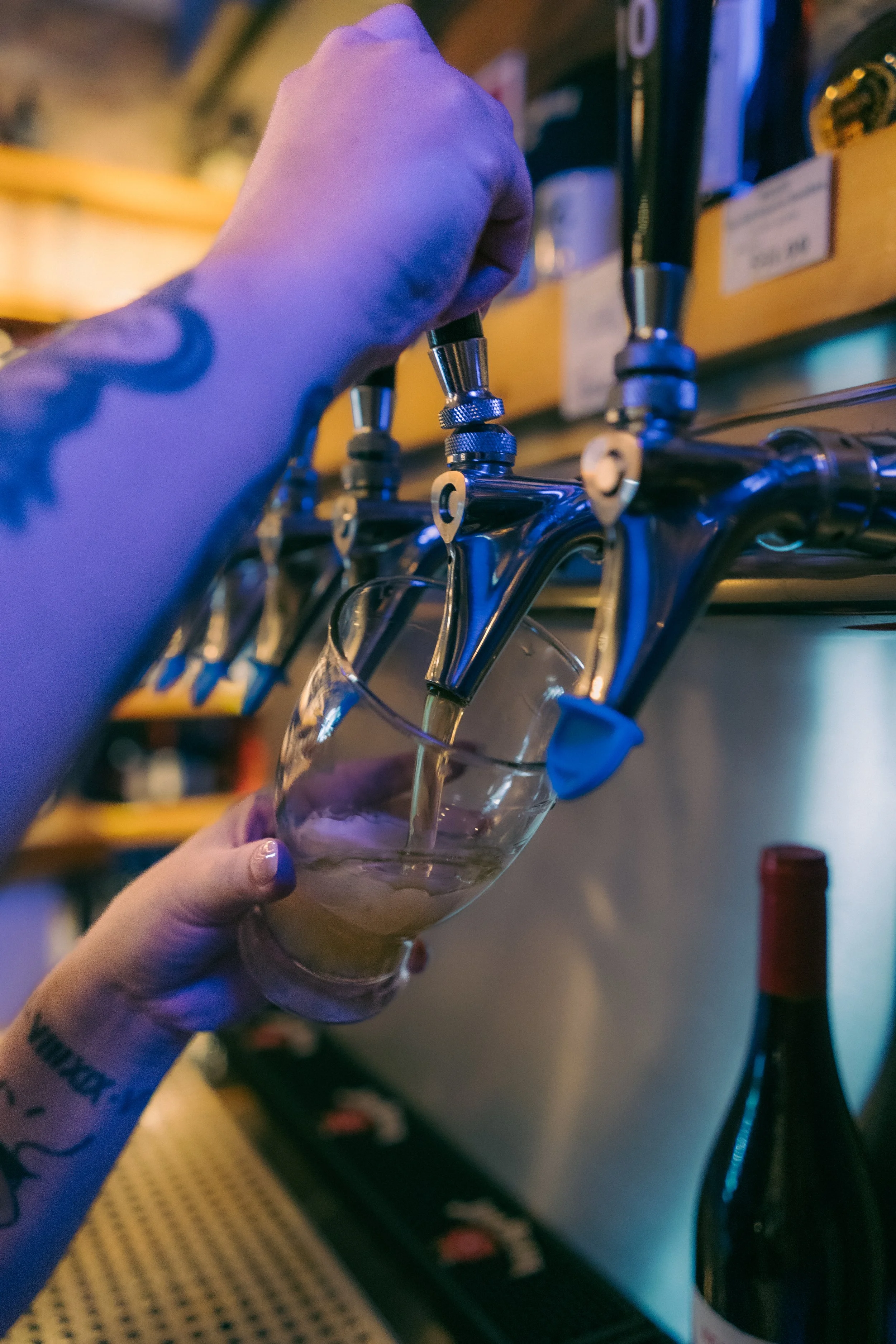 A person wearing a purple glove fills a glass with draft beer from a tap.