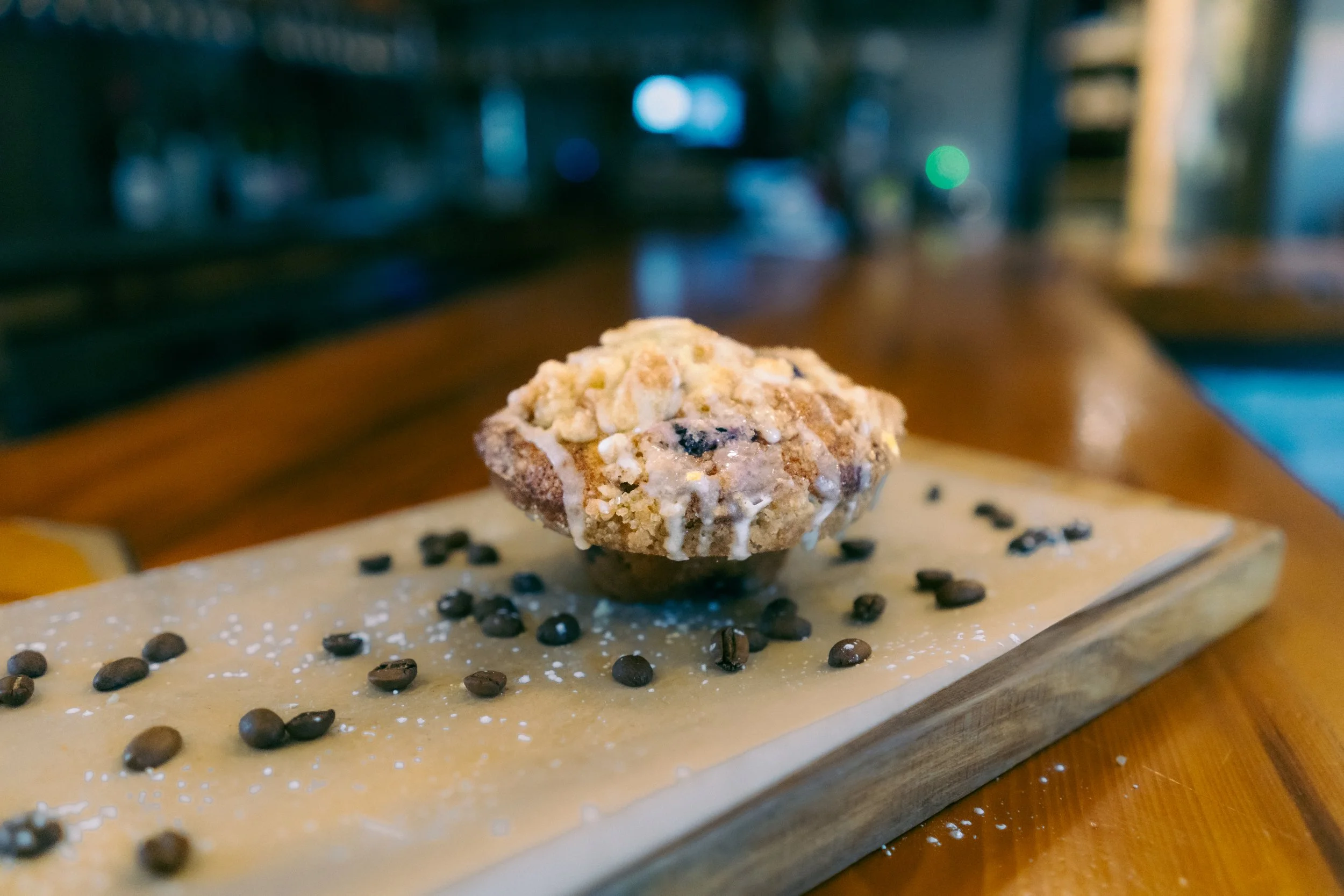 Chocolate muffin with crumb topping on a wooden serving board, sprinkled with chocolate chips and powdered sugar.
