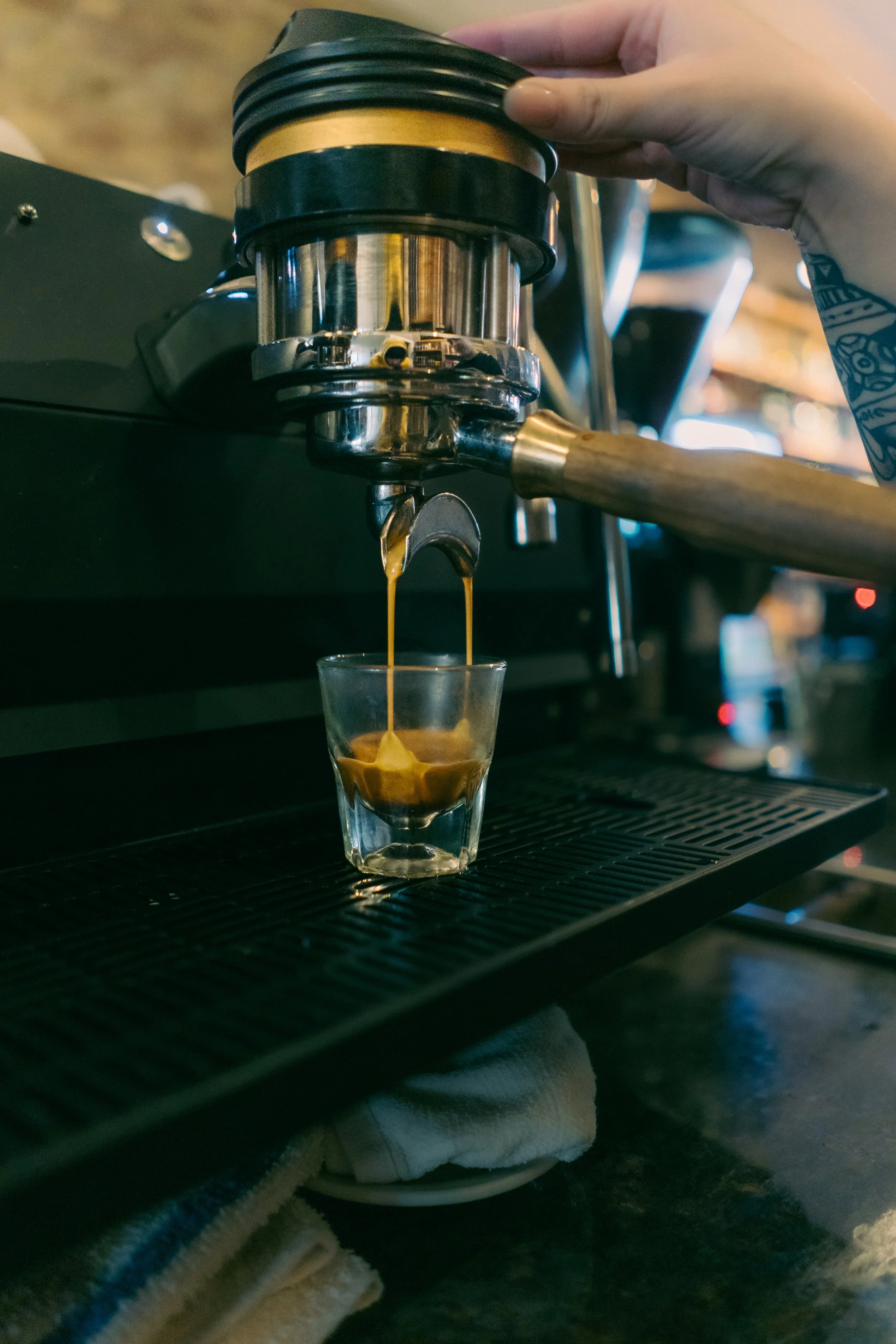 Close-up of a person using a portafilter to brew espresso on an espresso machine, with espresso dripping into a clear glass cup.