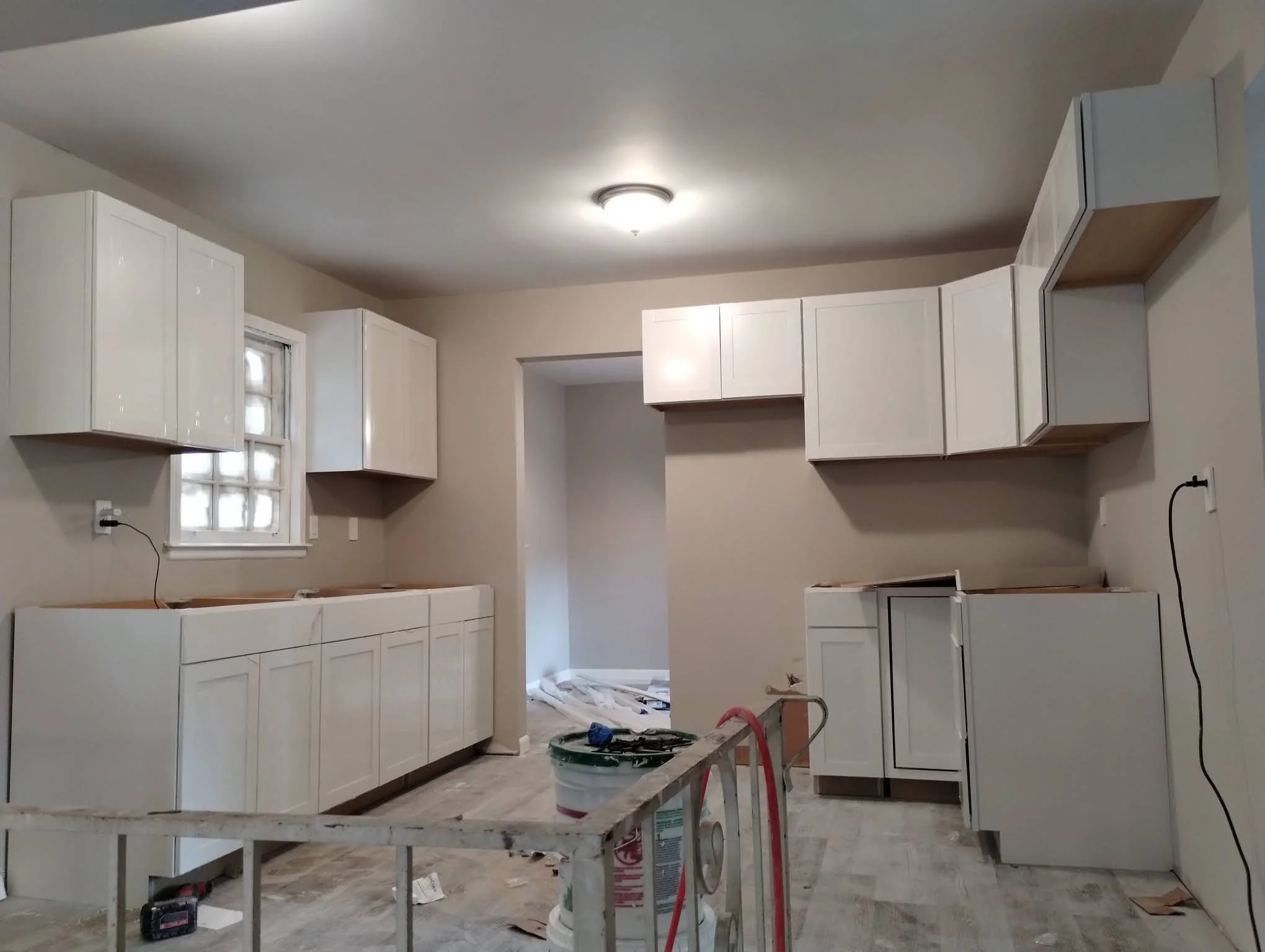 Kitchen under renovation with white cabinets, some not yet installed, and construction tools on the floor.