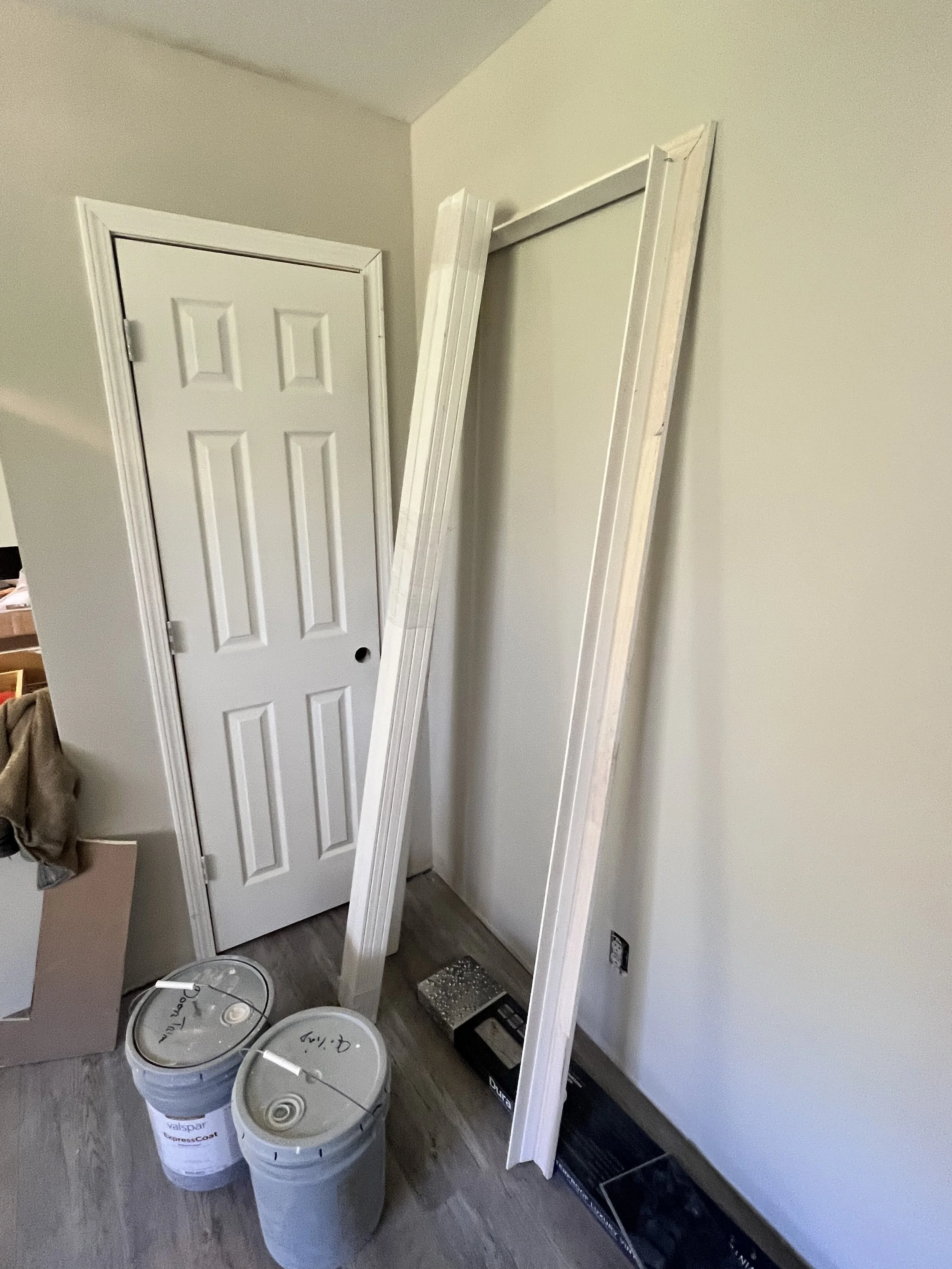 Room corner with door, drywall frame, paint cans, and box on the floor.