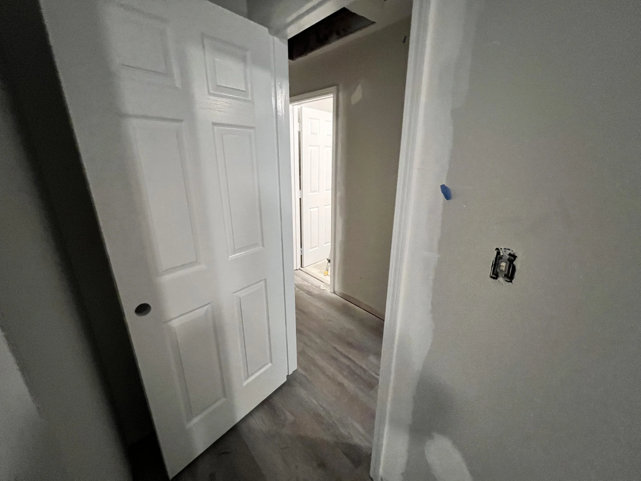 An interior room under construction with an open white door, unfinished walls, and electrical wiring without cover plates.