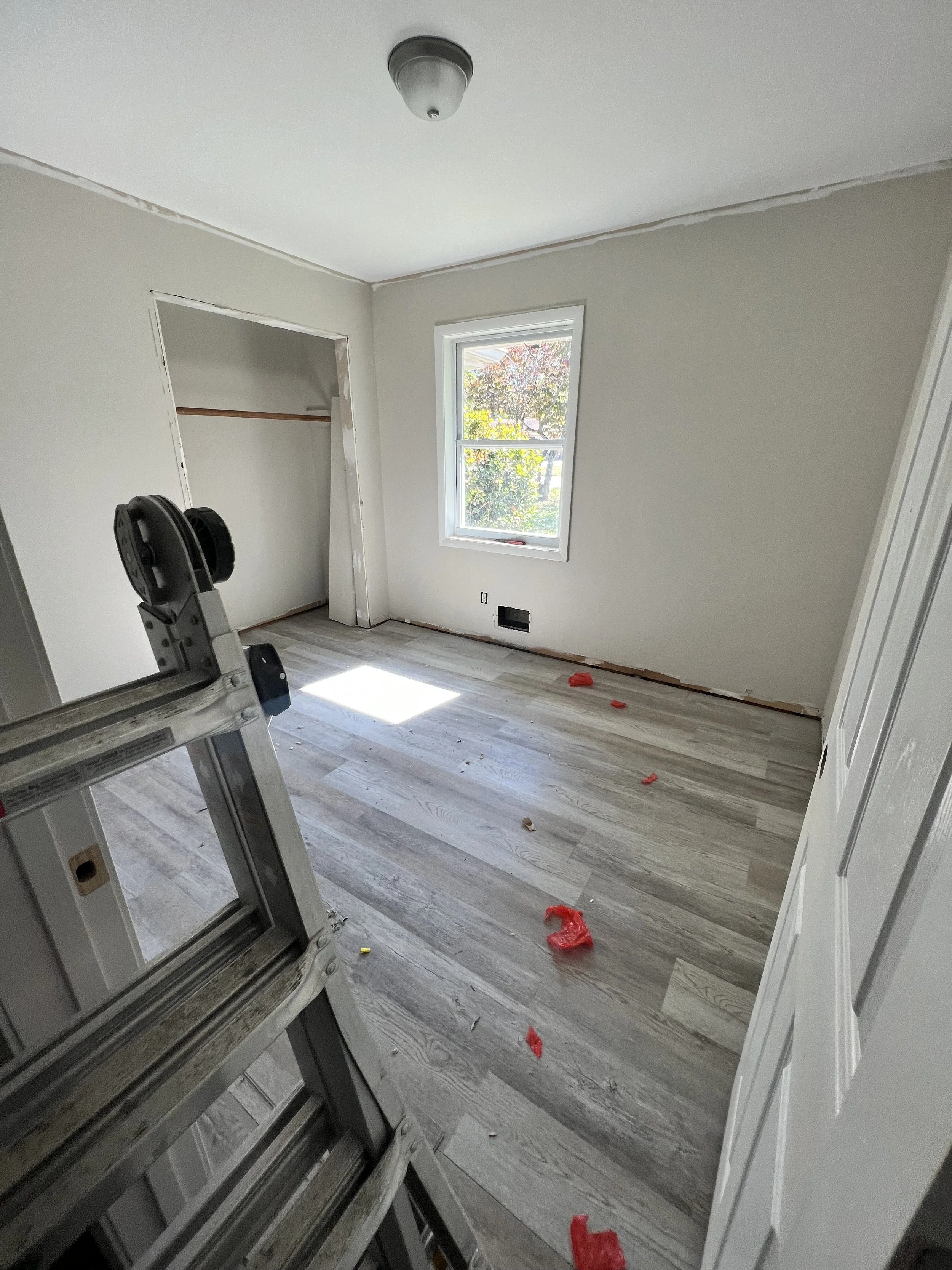 Empty room with a window, an open closet, a step ladder, and debris on the floor, indicating ongoing renovation or painting.