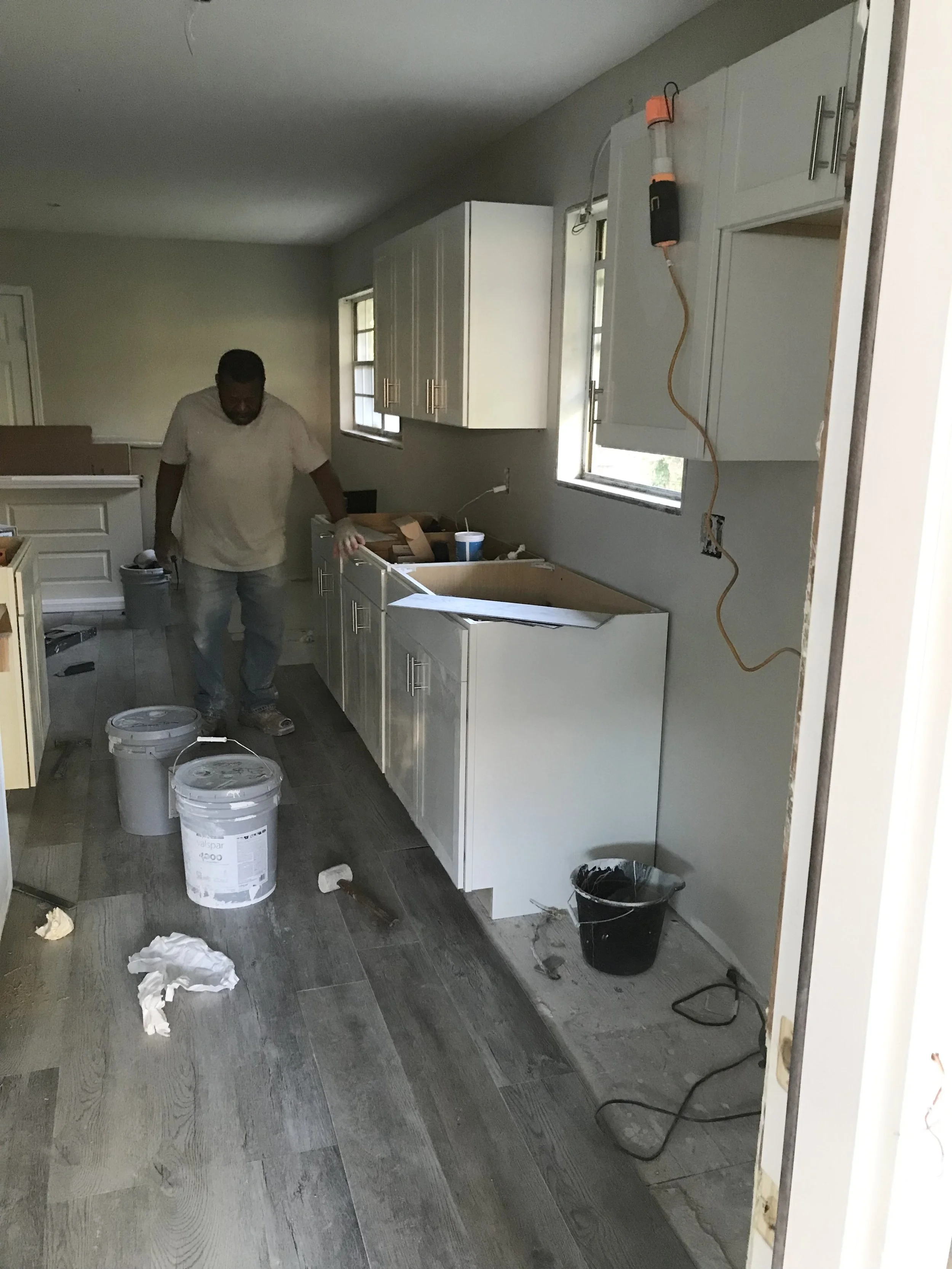 A person working on a kitchen renovation, with cabinets being installed and construction materials on the floor.