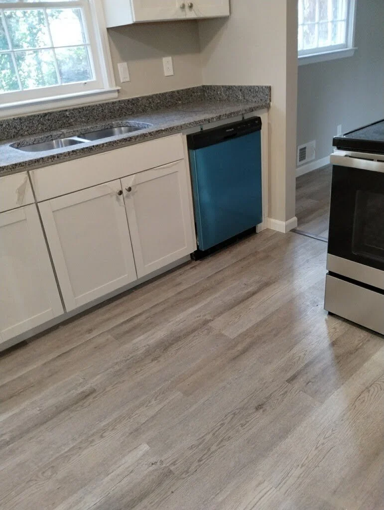 Kitchen with white cabinets, granite countertop, stainless steel sink, blue mini fridge, black stove, and wood-look flooring.