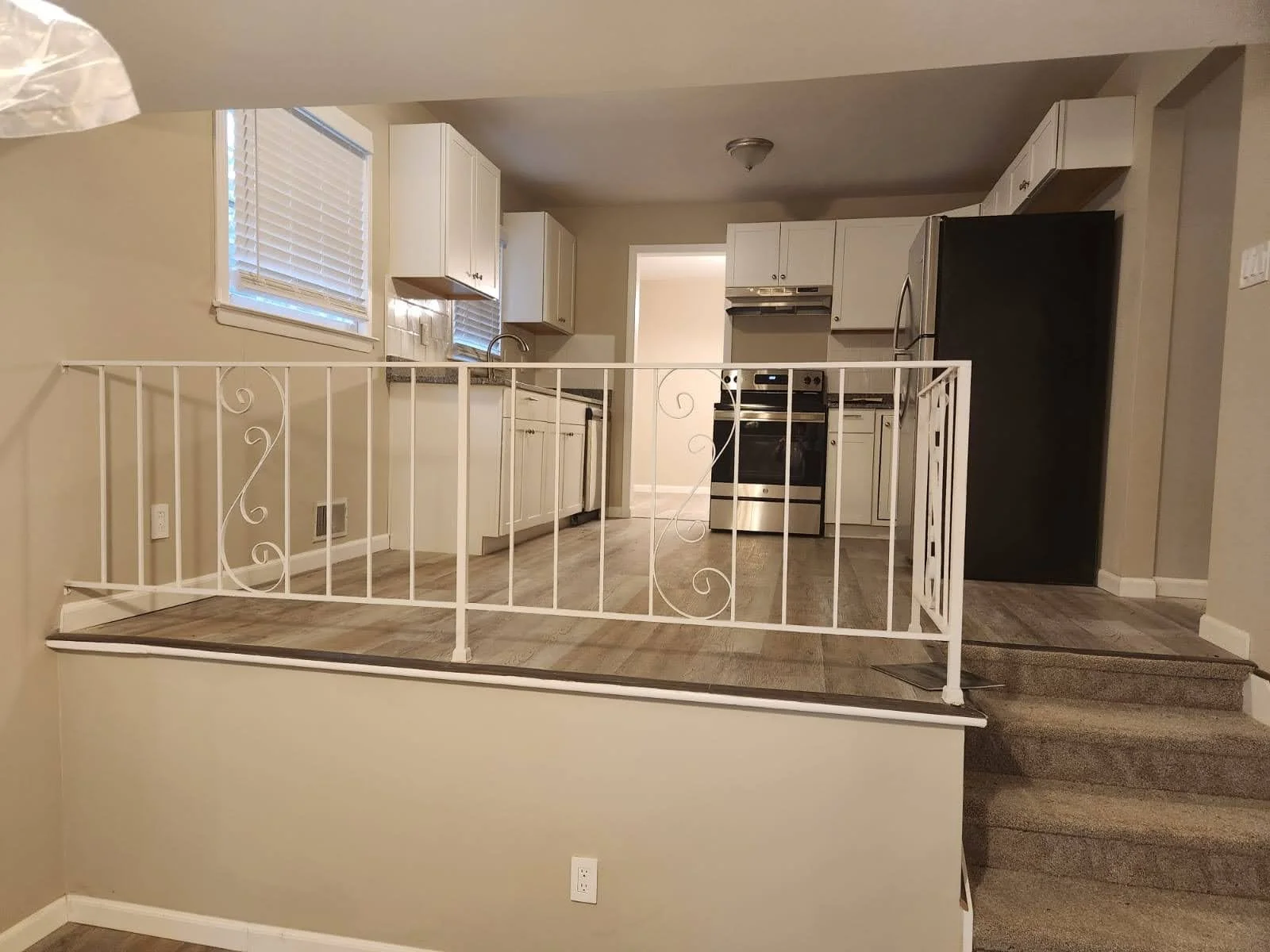 Kitchen with white cabinets, black refrigerator, stainless steel oven, and a white railing in front of the entrance to the kitchen area.