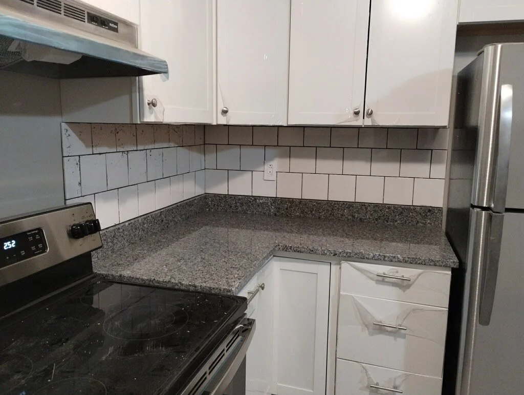 Kitchen corner with white cabinets, granite countertop, white tiled backsplash, stainless steel refrigerator, and stovetop
