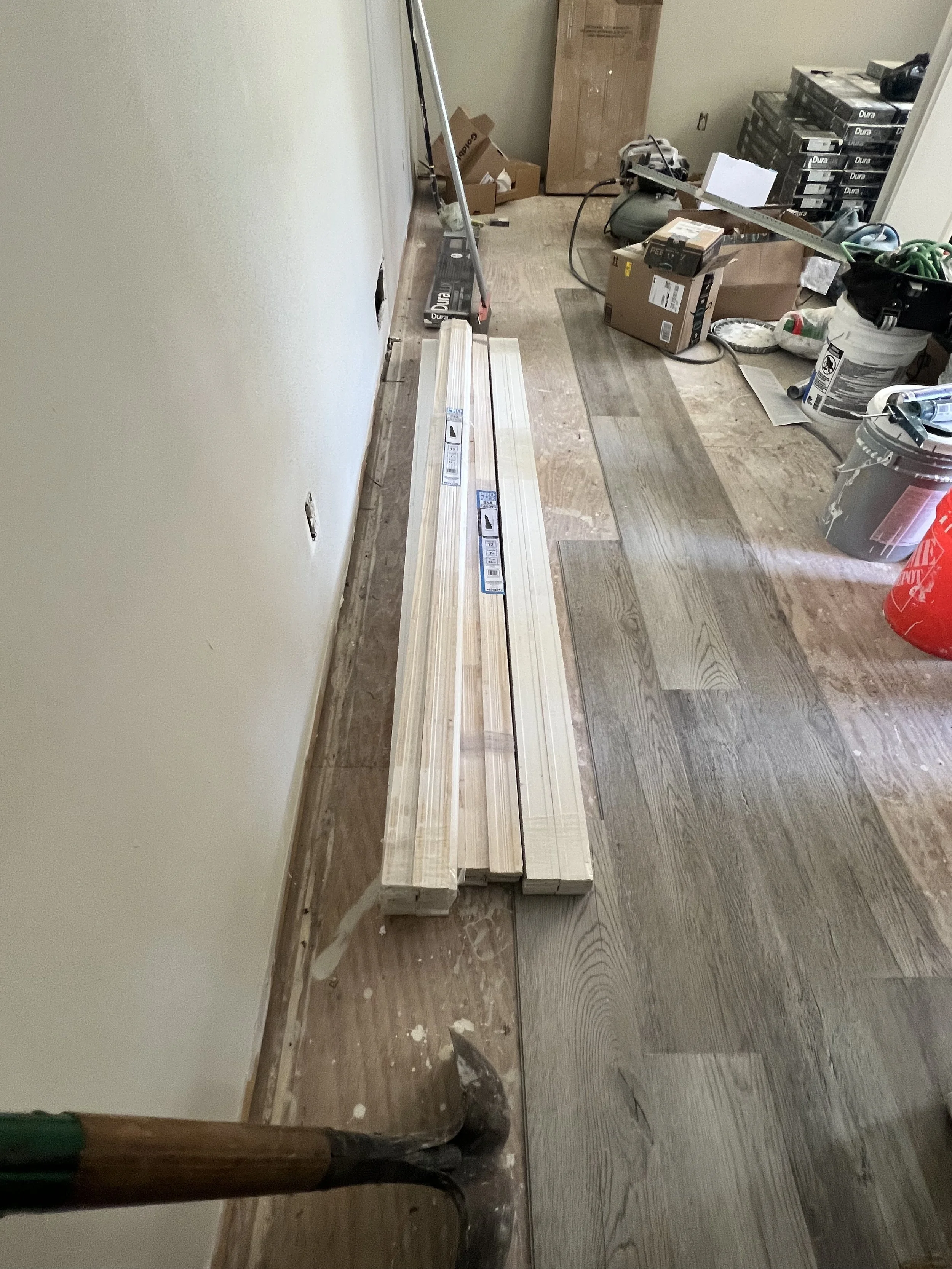 Lumber and construction tools in a room under renovation, with hardwood flooring and various building materials scattered around.