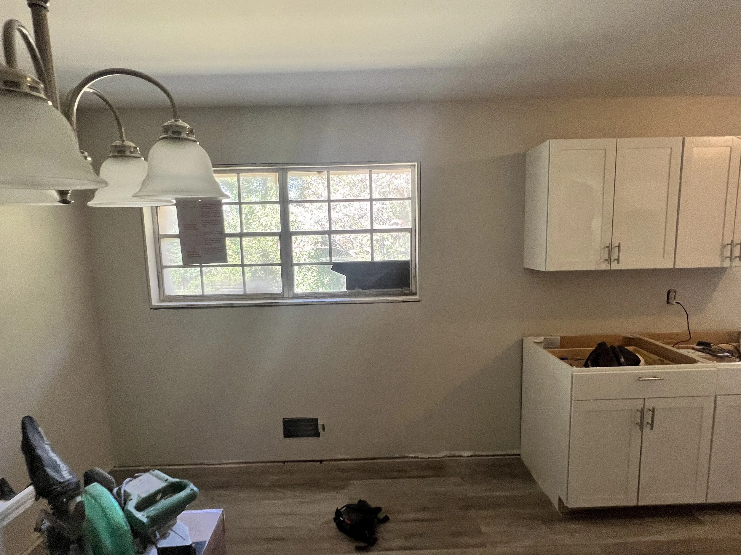A room in the process of renovation with unfinished kitchen cabinetry and a window with a view of trees outside.