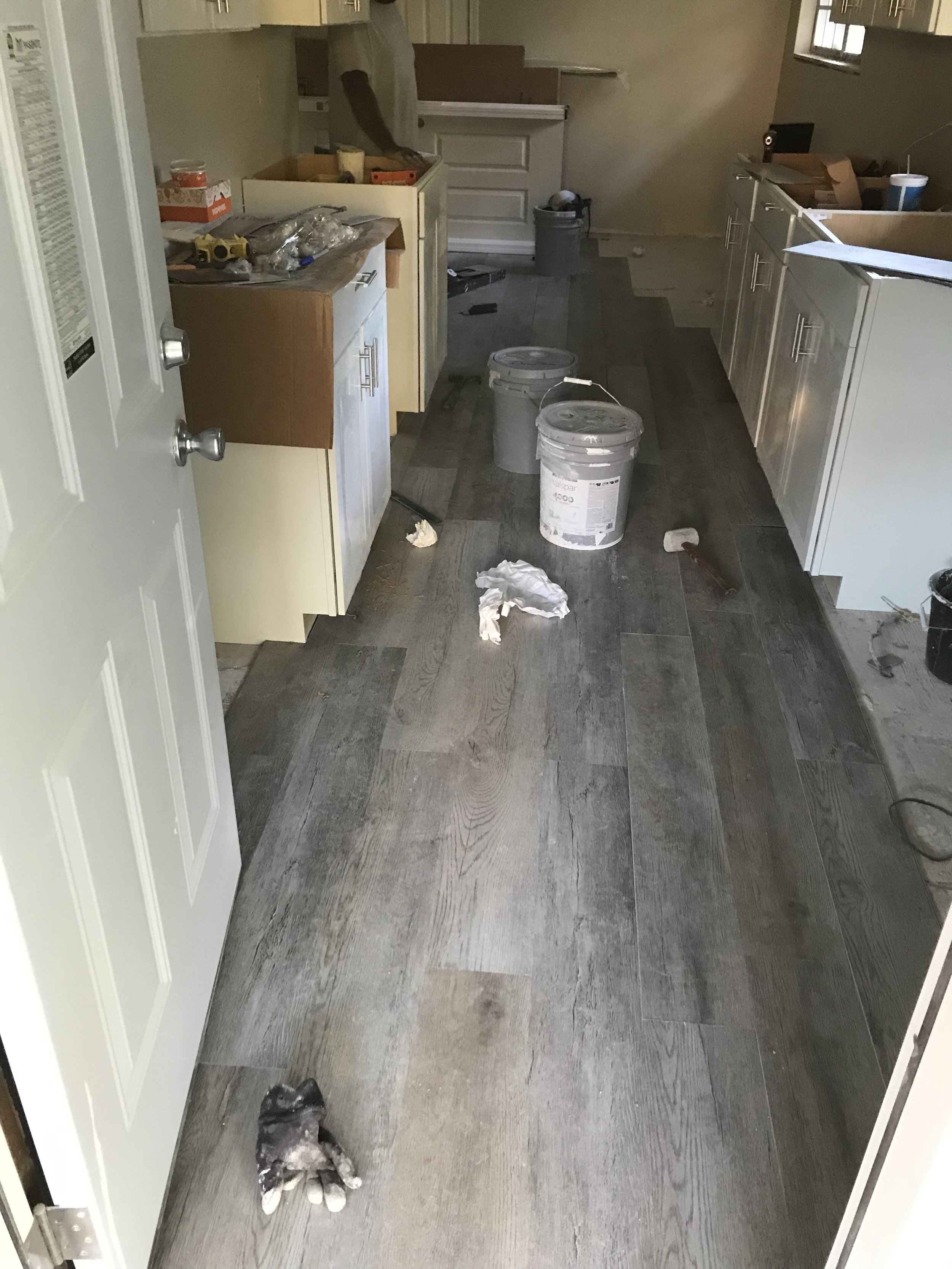 A kitchen under renovation with construction tools, paint buckets, and debris scattered on the floor.