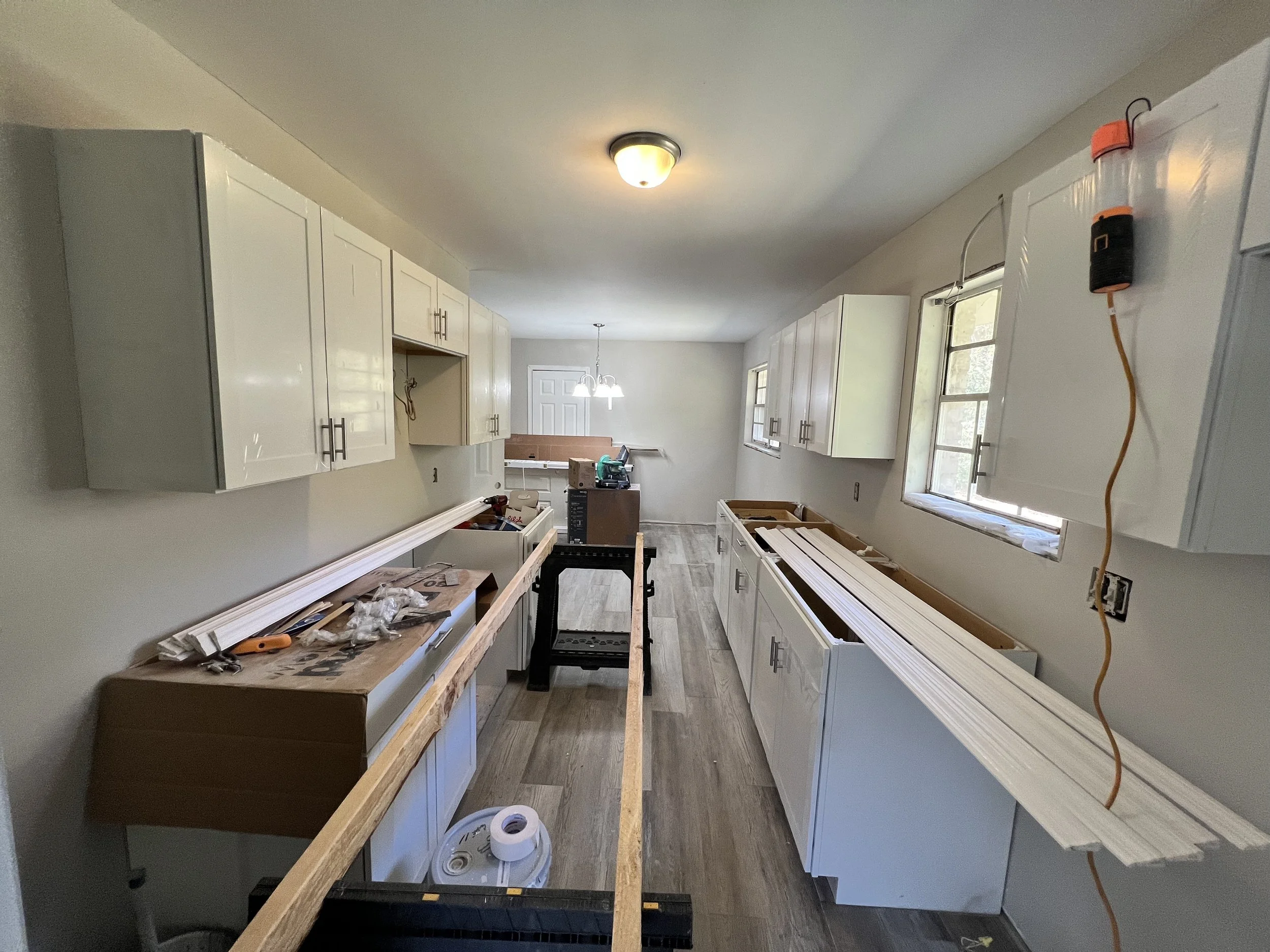 Kitchen under renovation with white cabinets, construction tools, and materials scattered around.