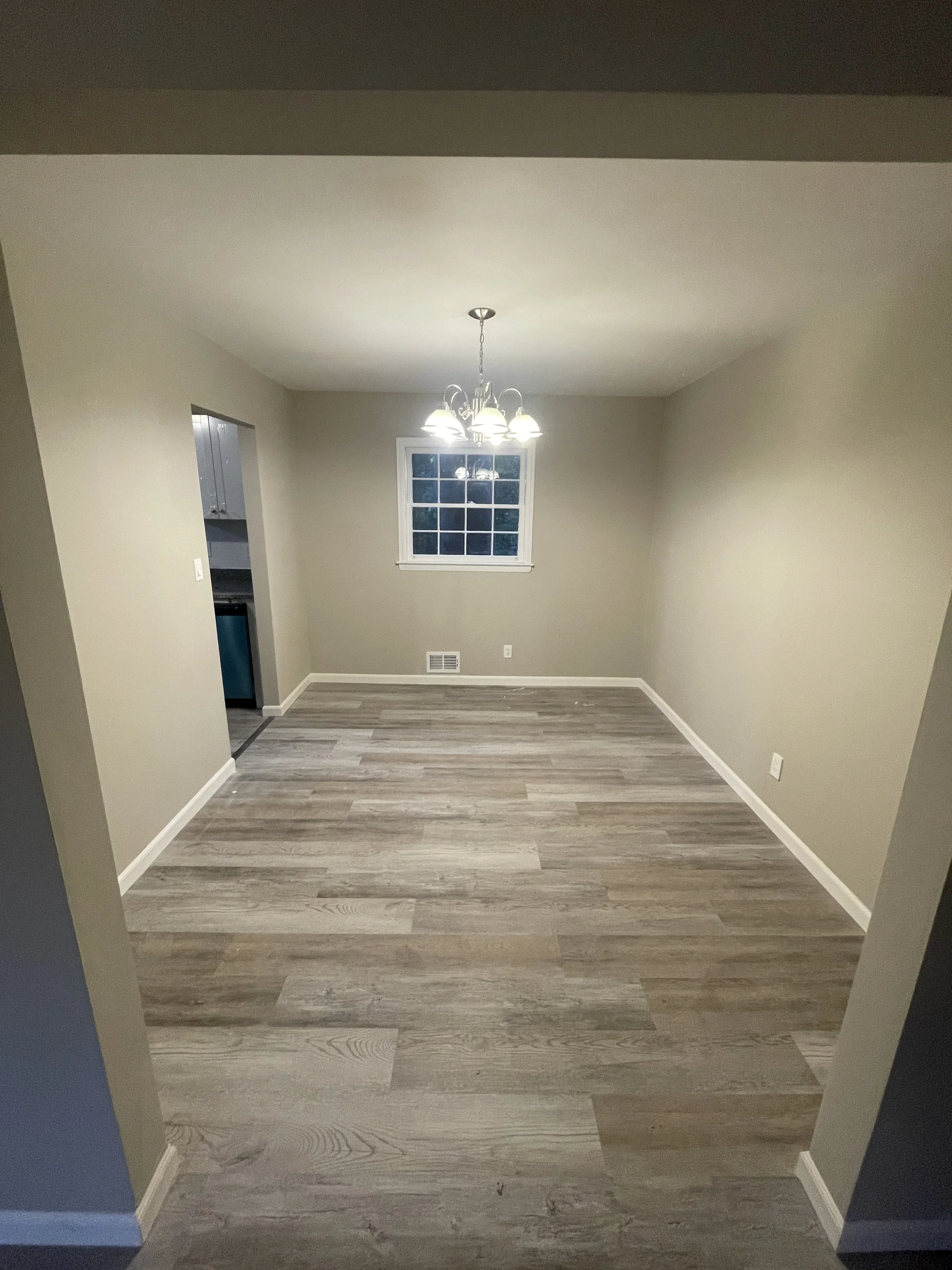 Empty dining room with beige walls, wooden flooring, a window, and a chandelier lighting fixture.
