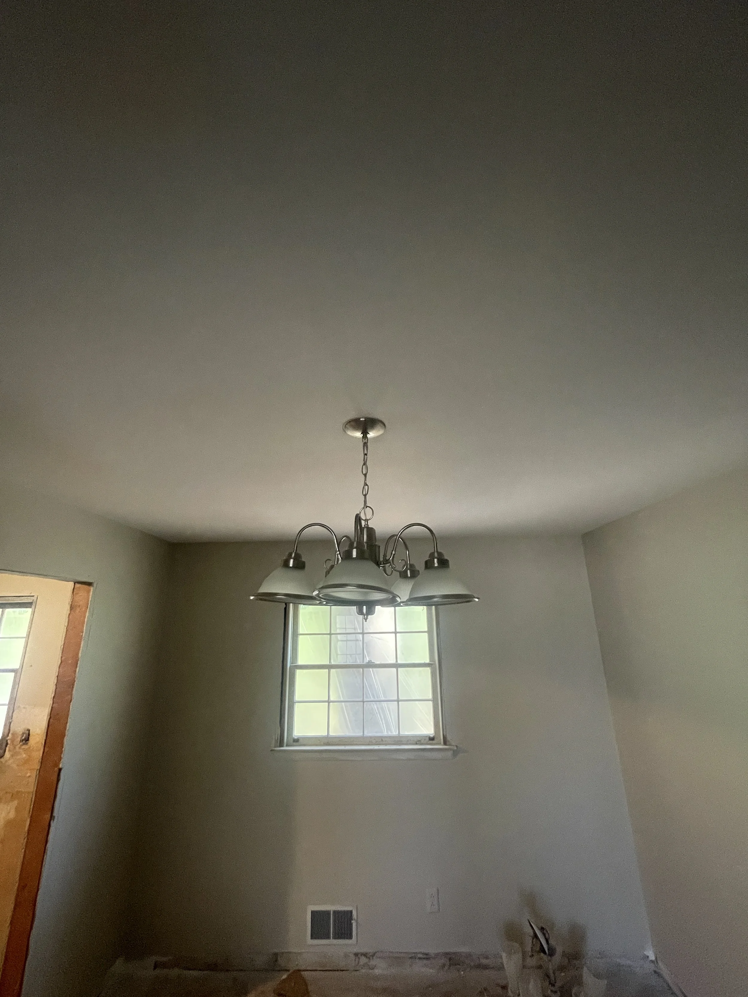 Empty room with a hanging ceiling light fixture and a window on the back wall.