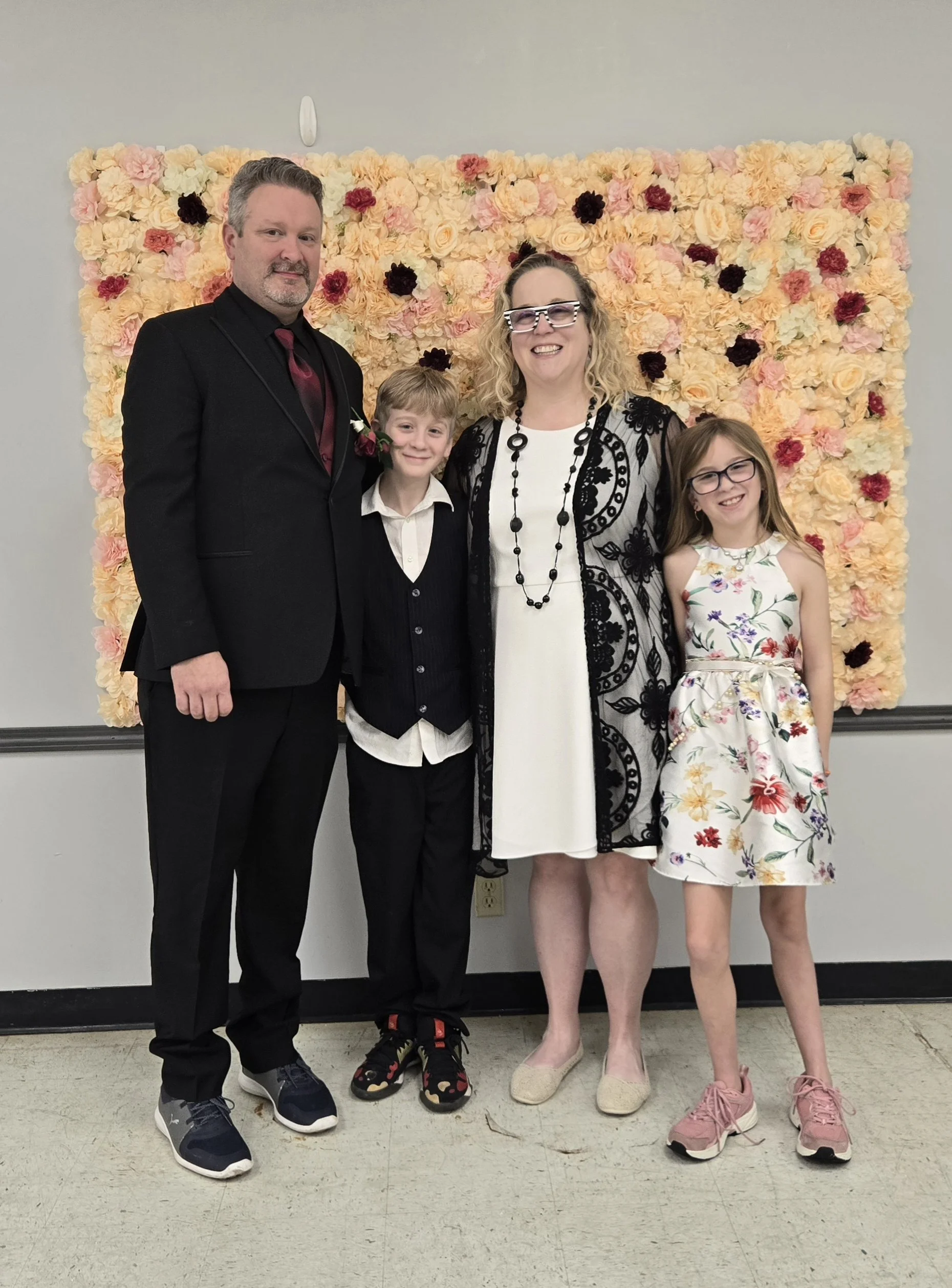 Family of four posing in formal attire in front of a pastel flower wall