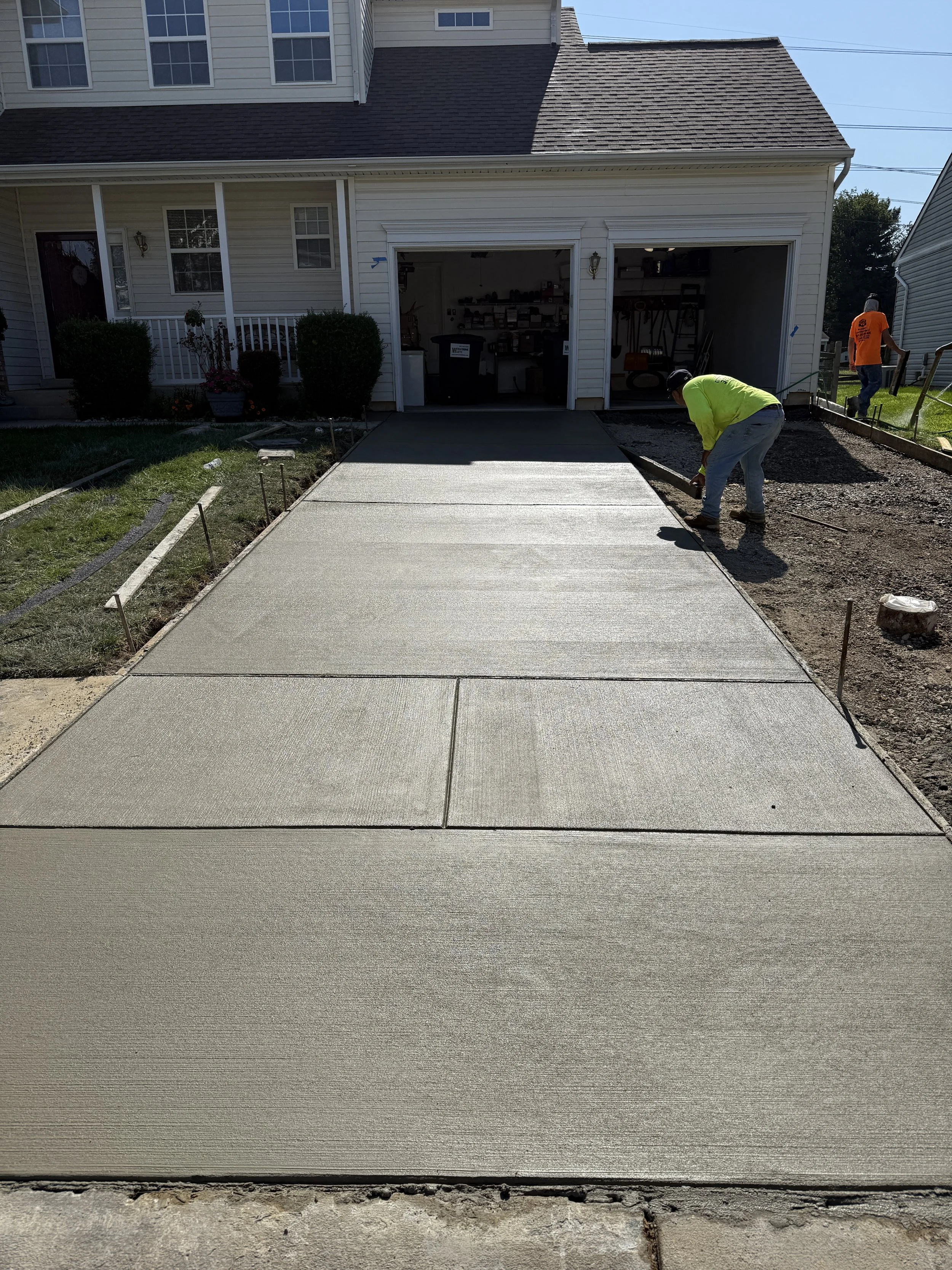 Workers pouring fresh concrete for a new driveway in front of a house.