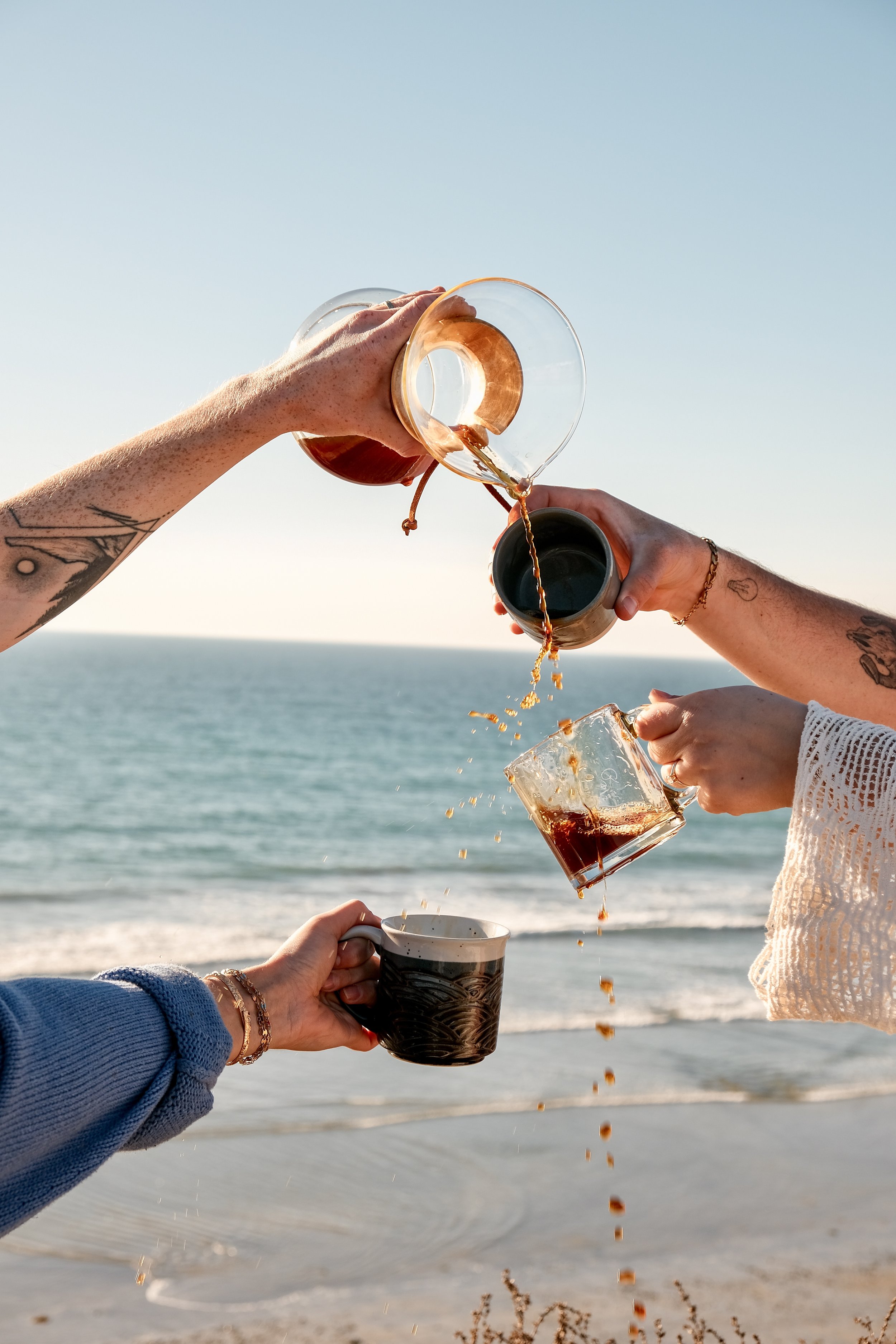 Layered coffee pour cascading between glass carafe, mug, and cup with the San Diego coastline in the background