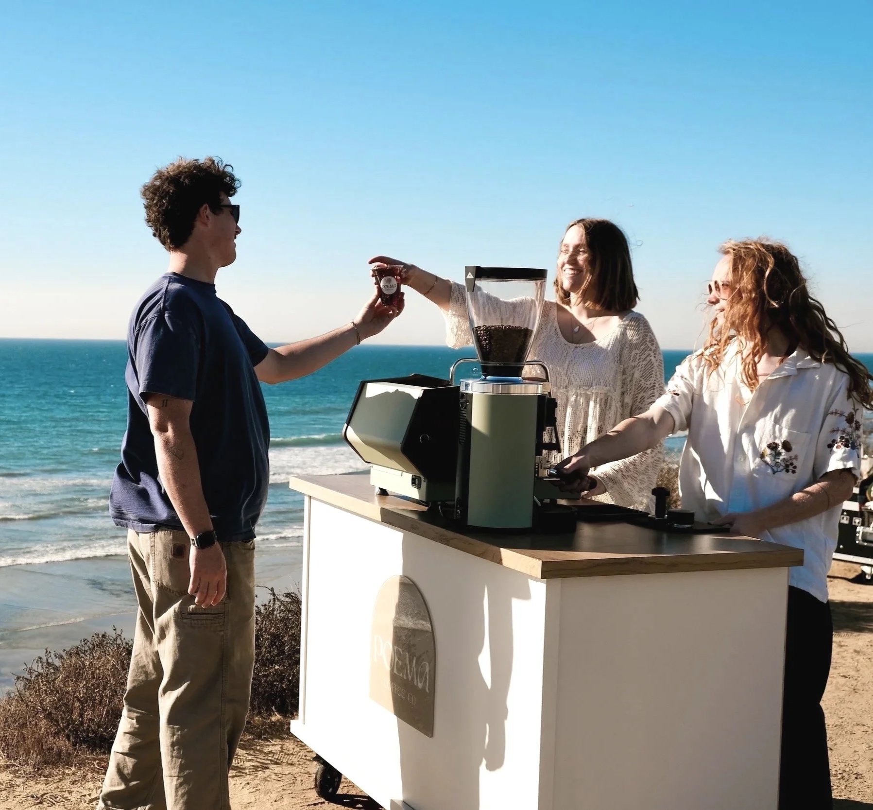 Barista serving coffee from a mobile cart by the ocean in San Diego