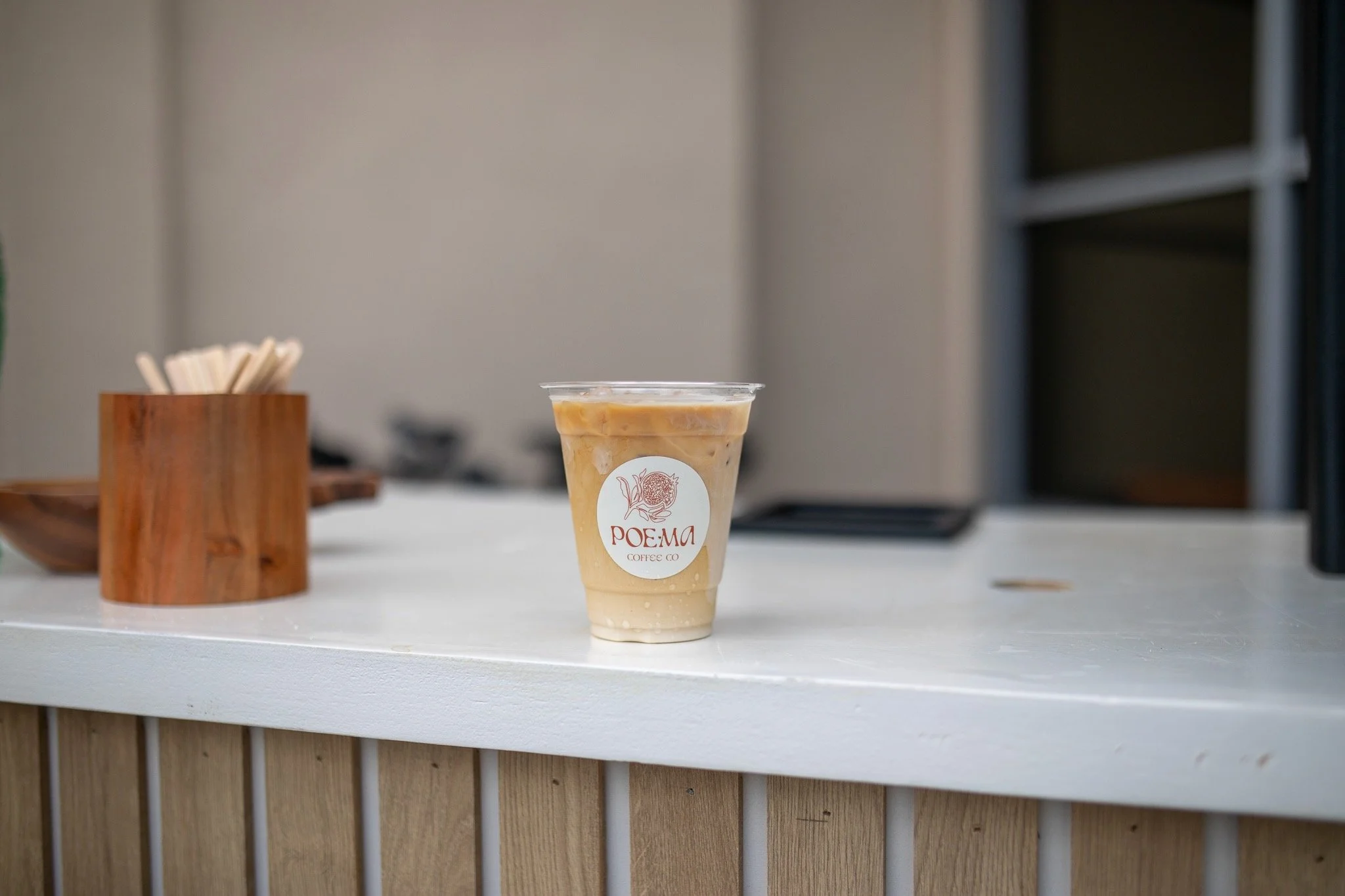 Iced latte with Poema Coffee Co logo on a white coffee bar, showcasing premium craft coffee, minimalist branding, and modern espresso catering design.