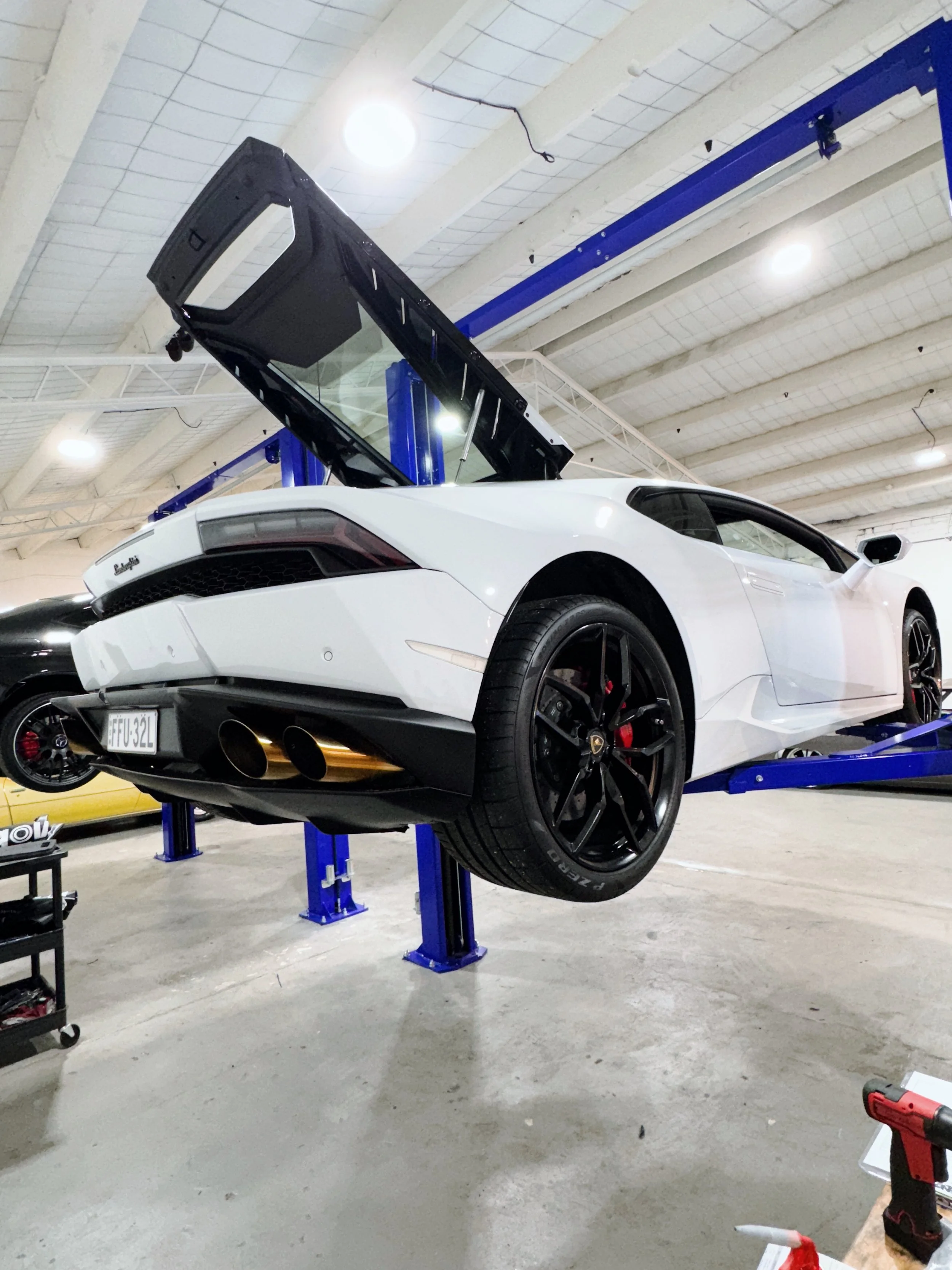 White Lamborghini sports car elevated on a blue hydraulic lift in a garage or workshop.