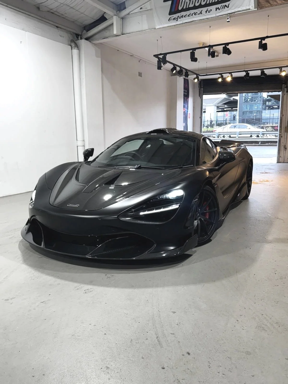 Gray sports car with upward-opening door in a dimly lit garage.