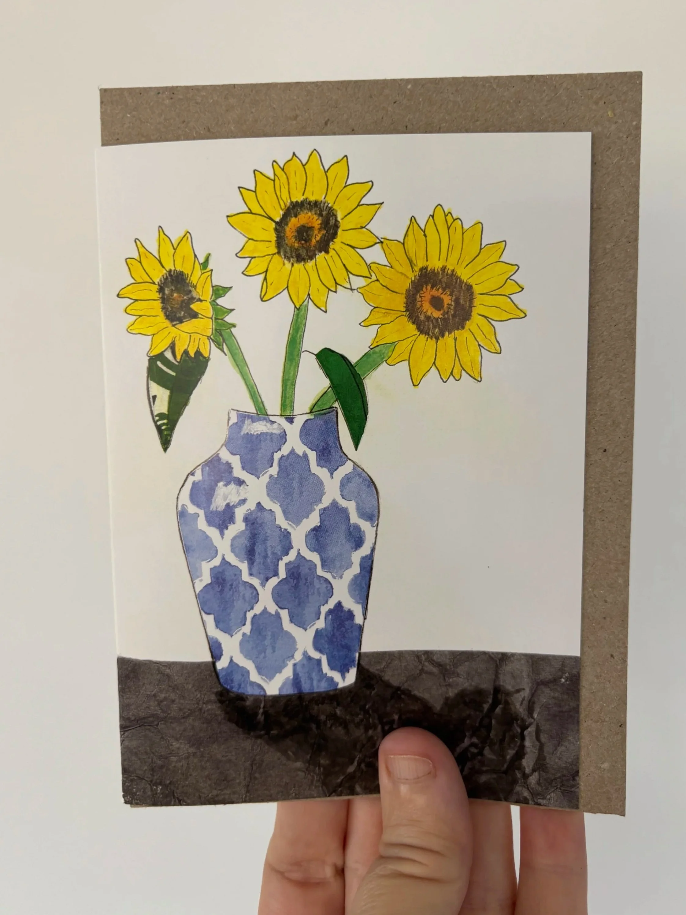 Greeting card featuring a watercolour, ink and collage image of sunflowers in a blue vase.