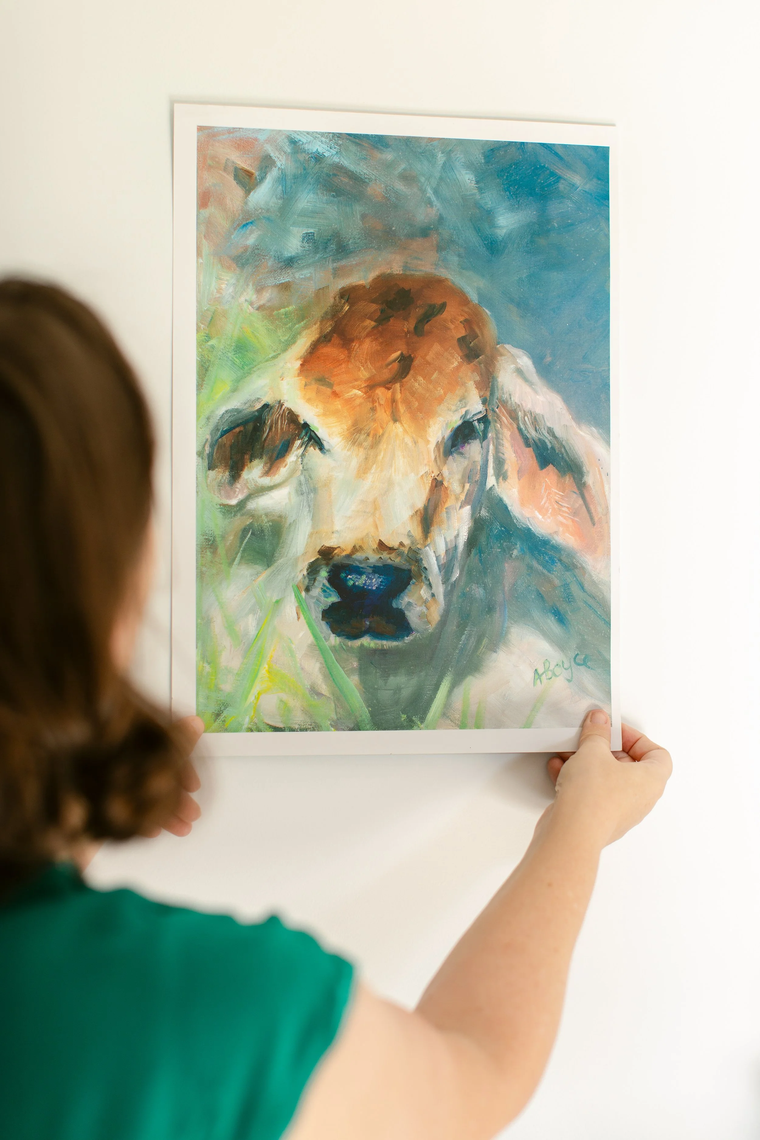 A person holding a colorful painting of a dog's face on a white wall.