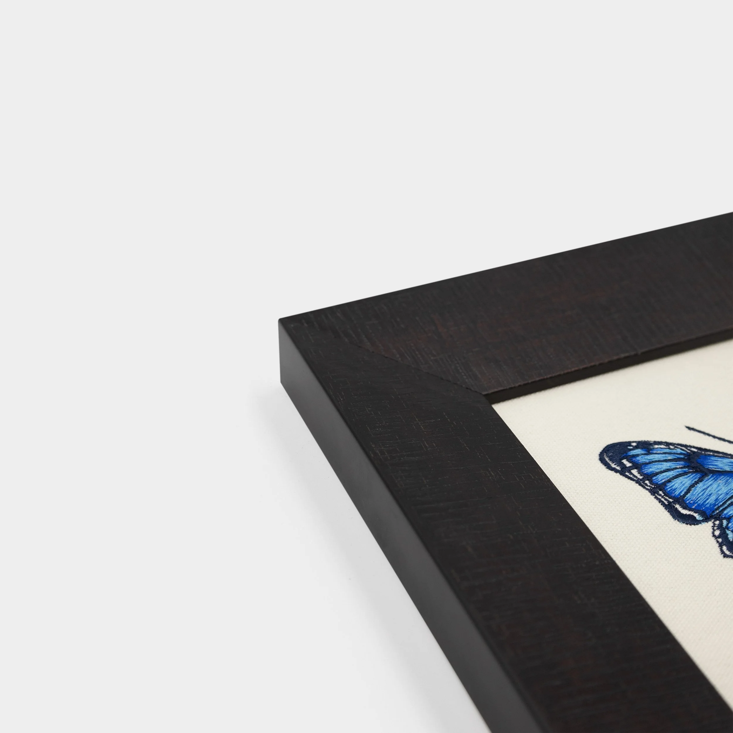 Corner detail of the substantial dark solid wood frame used on the Nocturna butterfly embroidered wall art